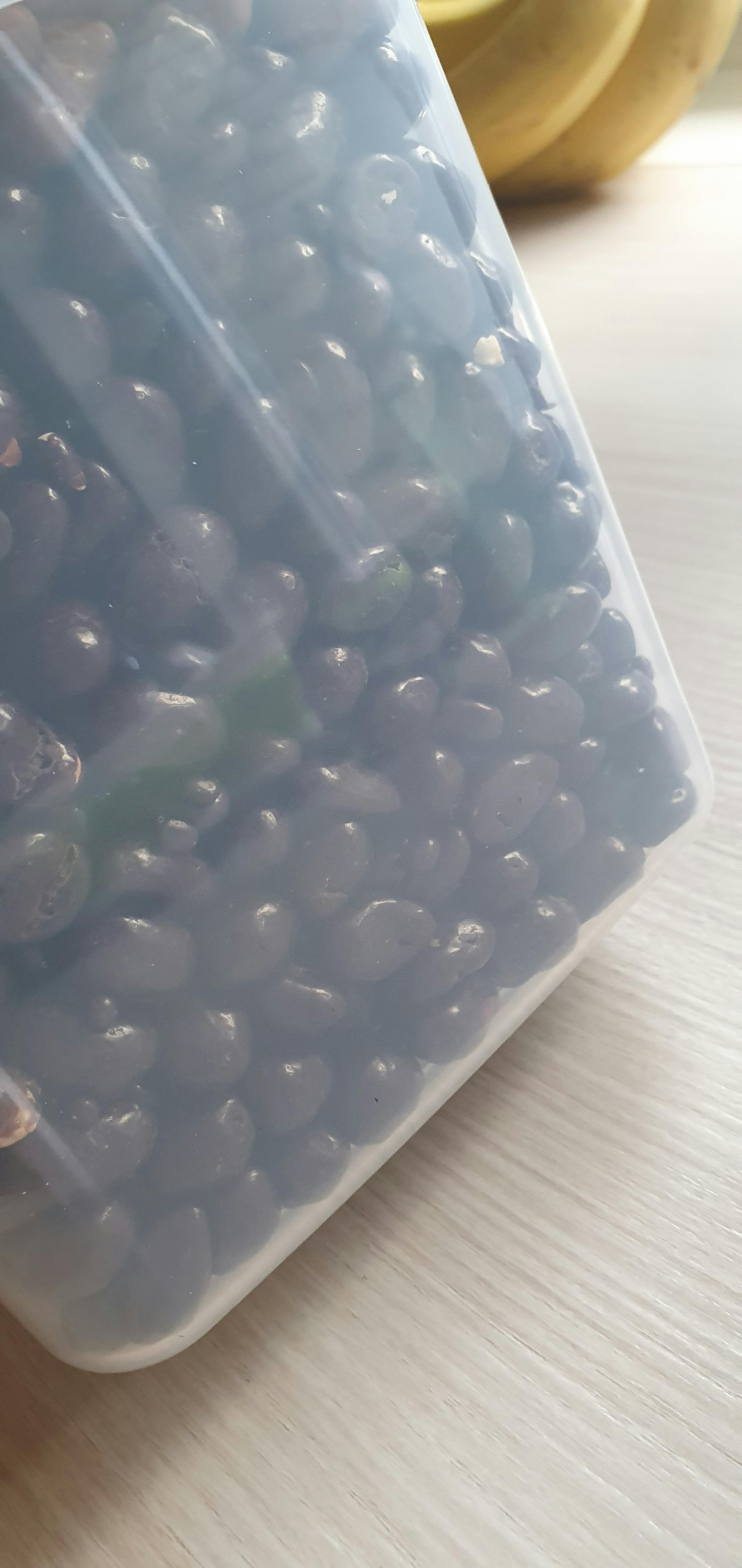 ein Plastikbehälter gefüllt mit schwarzen Beeren auf einem Tisch