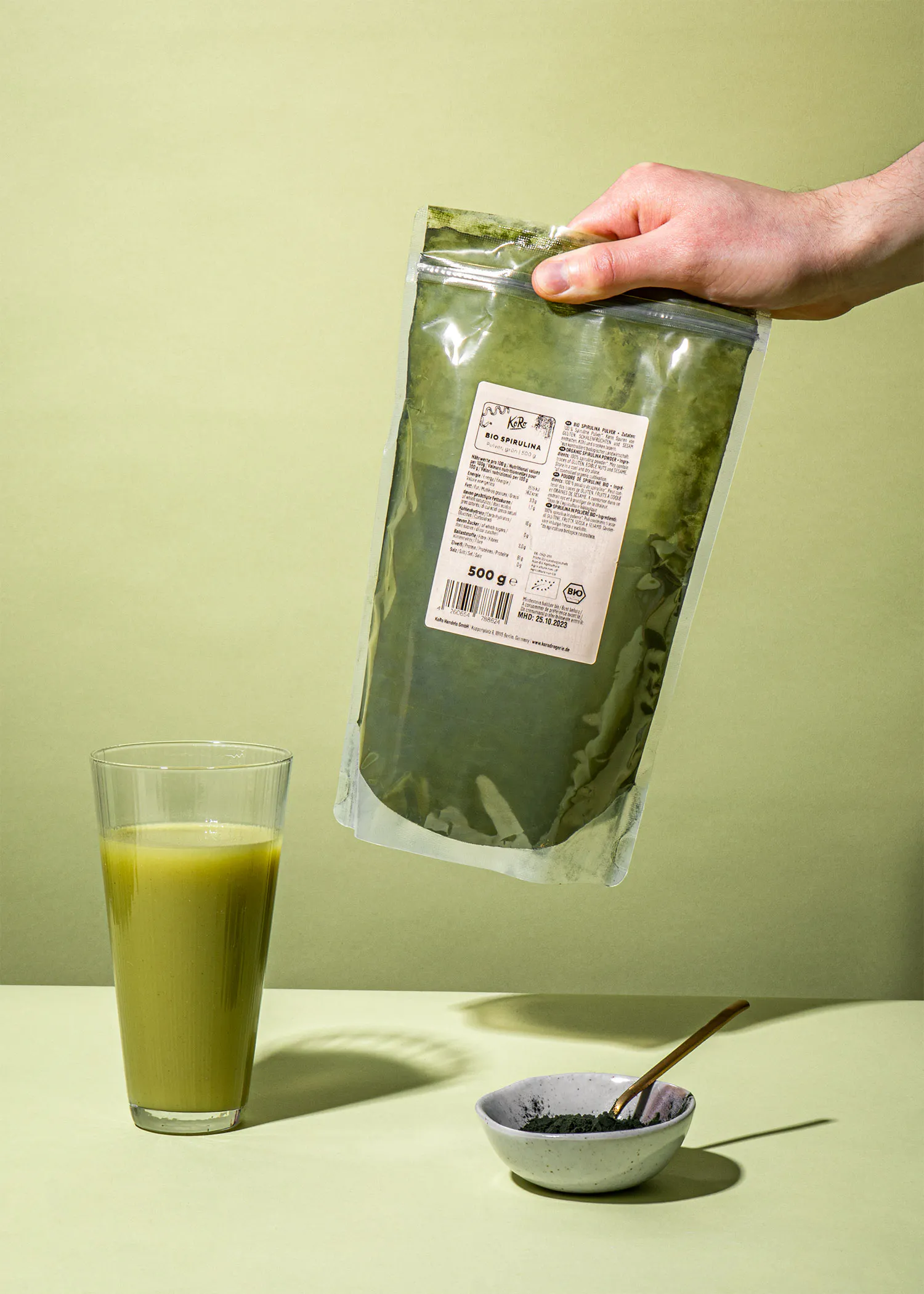 une personne tient un sac de poudre à côté d' un verre de boisson verte