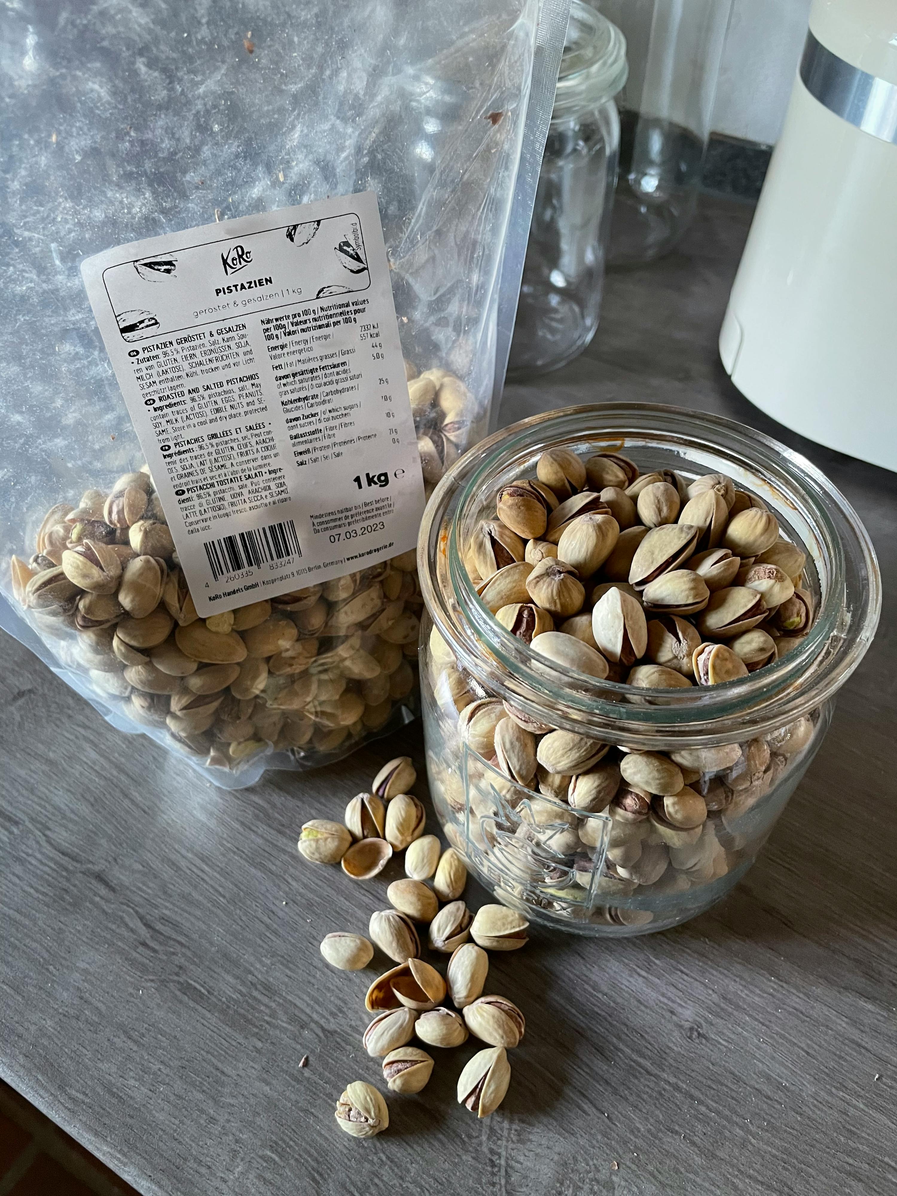 ein Glas gefüllt mit pistazien neben einem Plastikbeutel mit pistazien