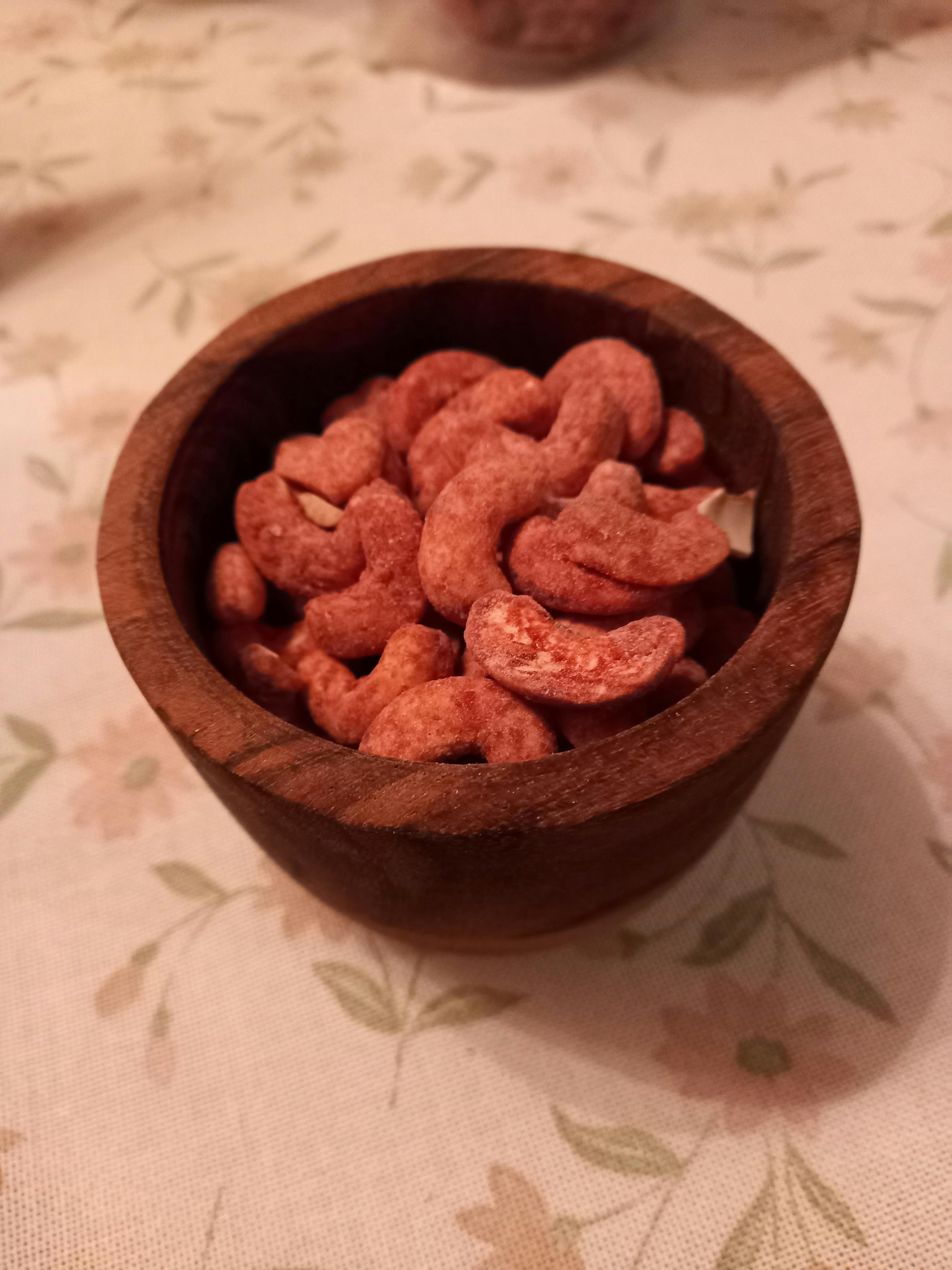 eine Holzschale mit roten Cashewnüssen auf einem Tisch