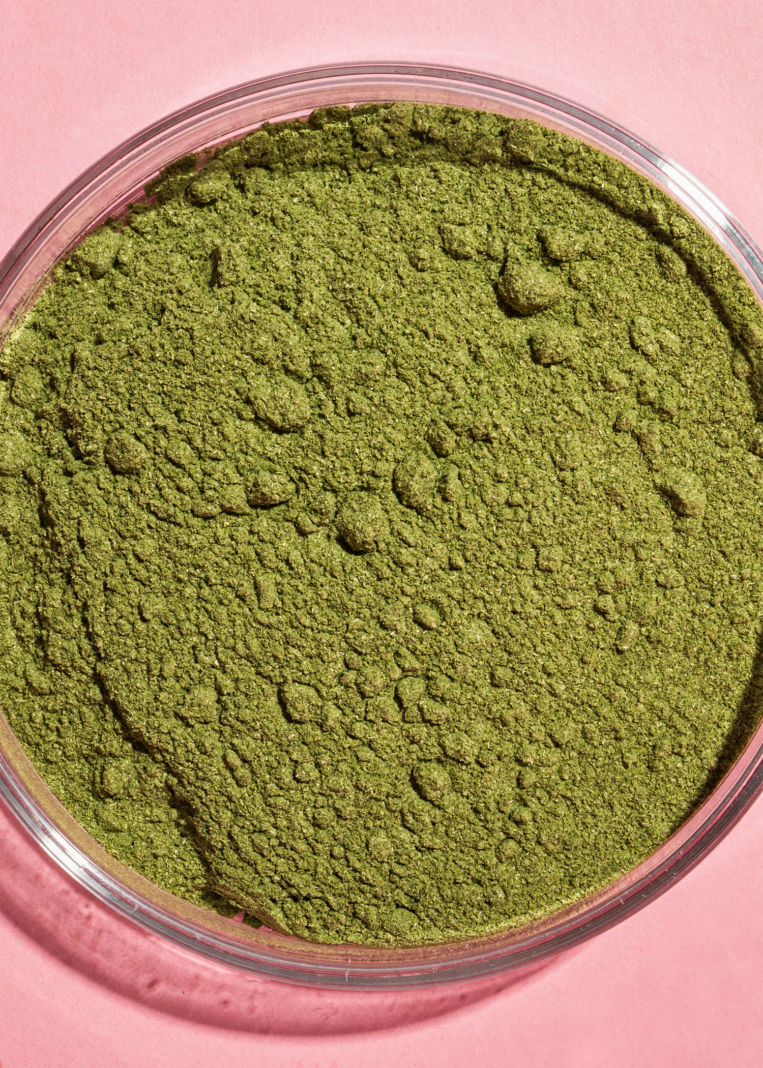 un bol en verre rempli de poudre verte sur un fond rose
