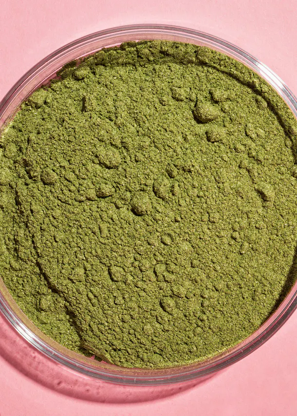 un bol en verre rempli de poudre verte sur un fond rose