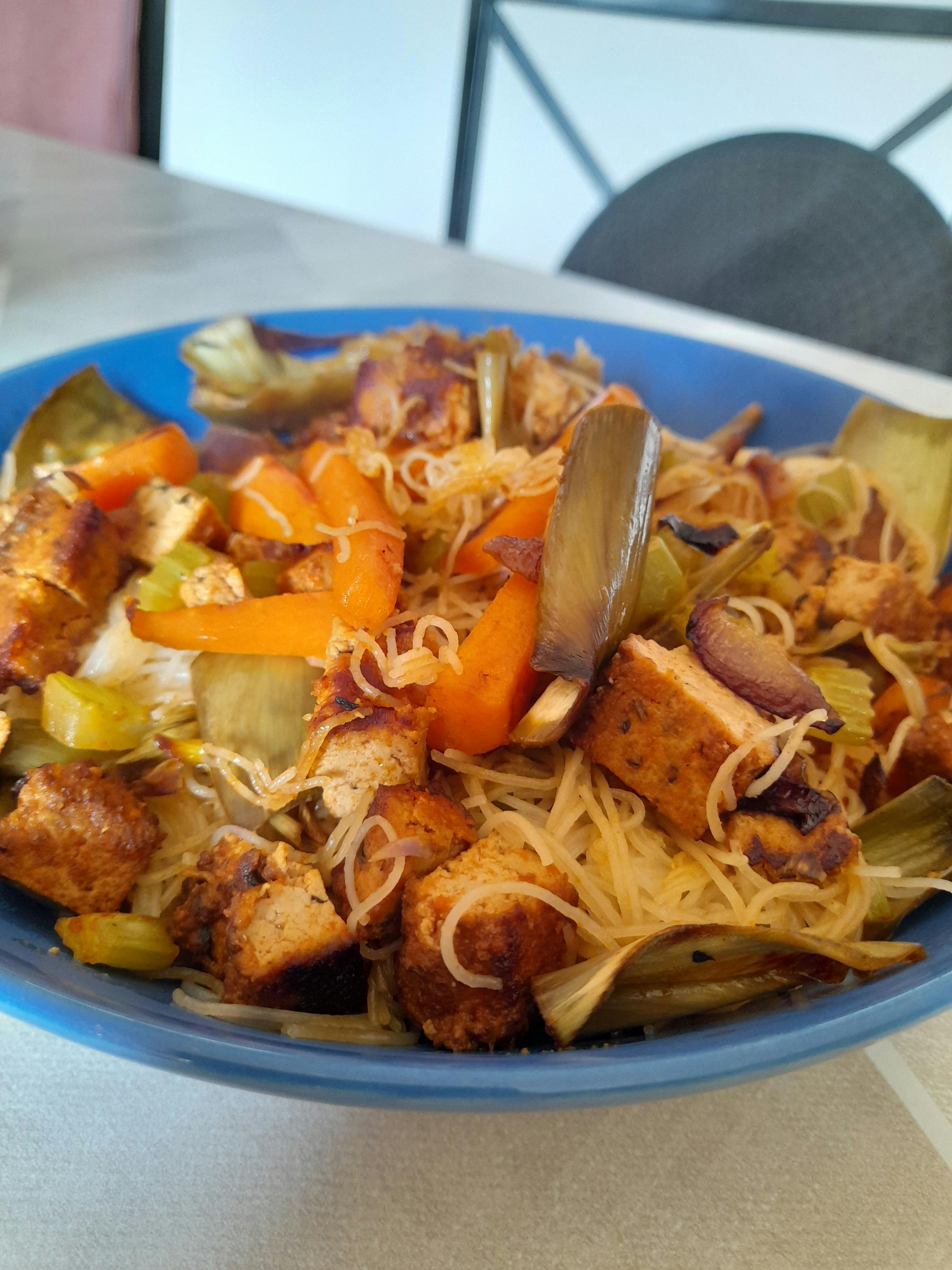 ein blauer Teller mit Nudeln und Gemüse steht auf einem Tisch