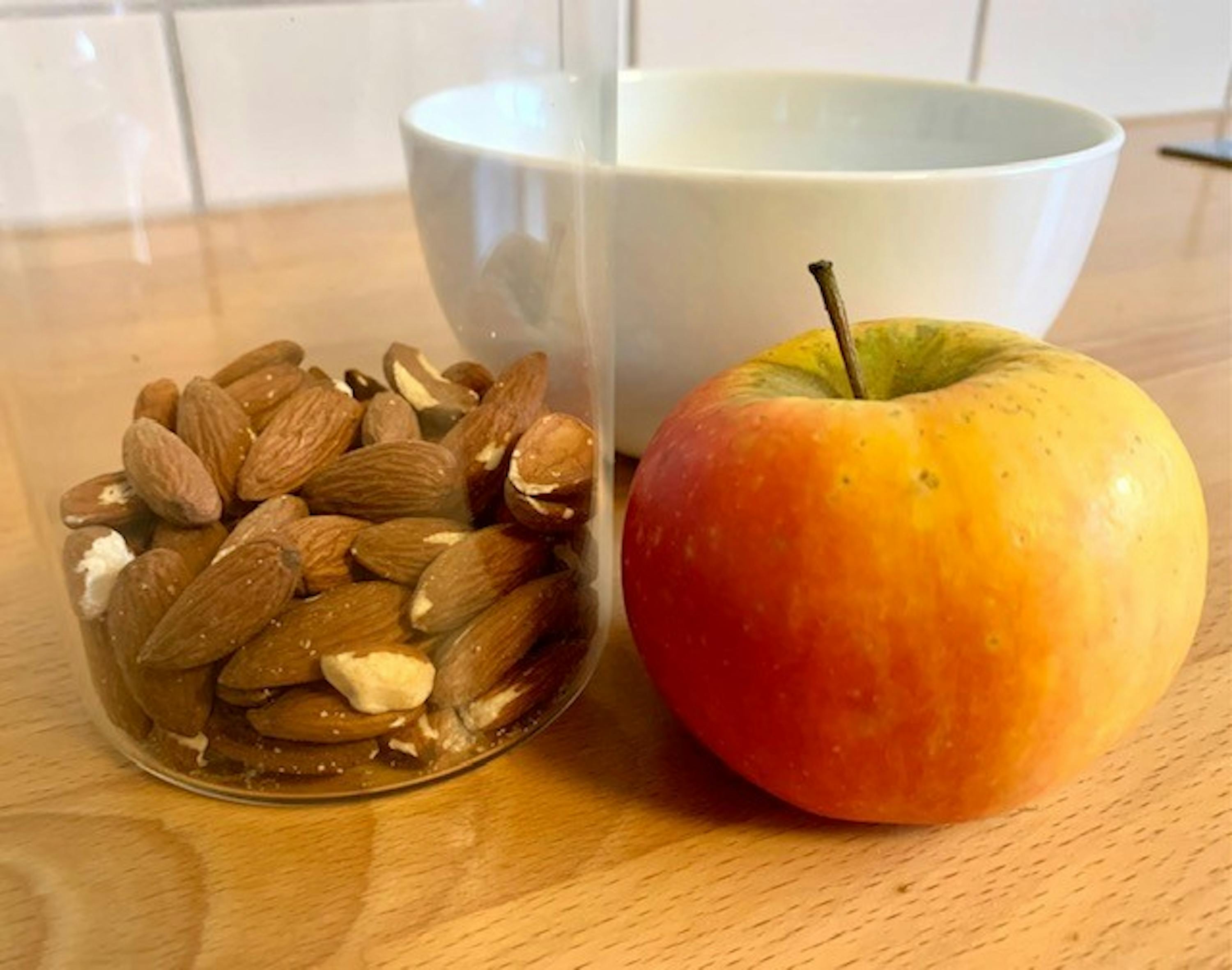 an apple next to a jar of almonds on a table