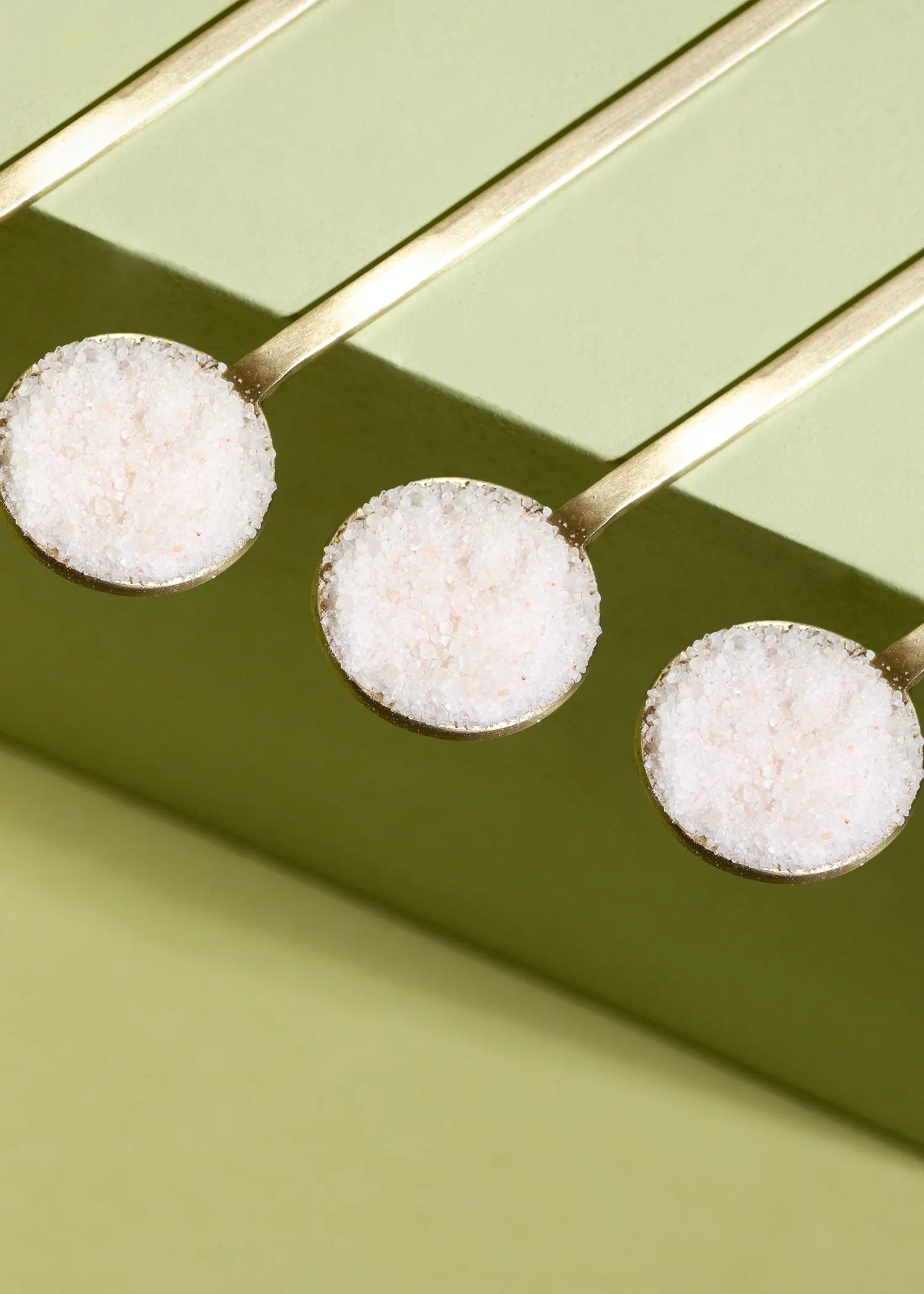 trois cuillères remplies de sel sont alignées sur une surface verte