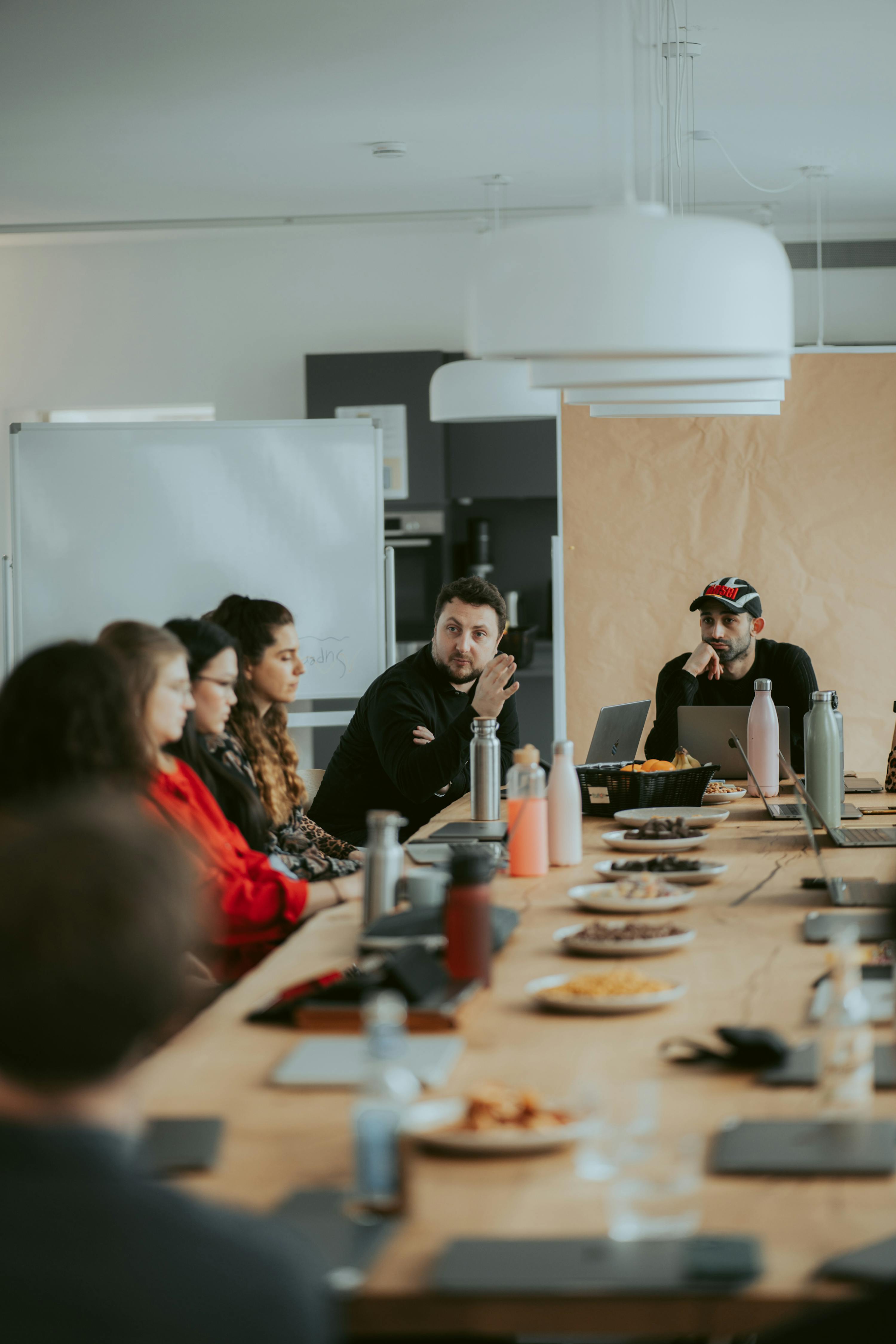 un gruppo di persone si siede attorno a un lungo tavolo con piatti e laptop