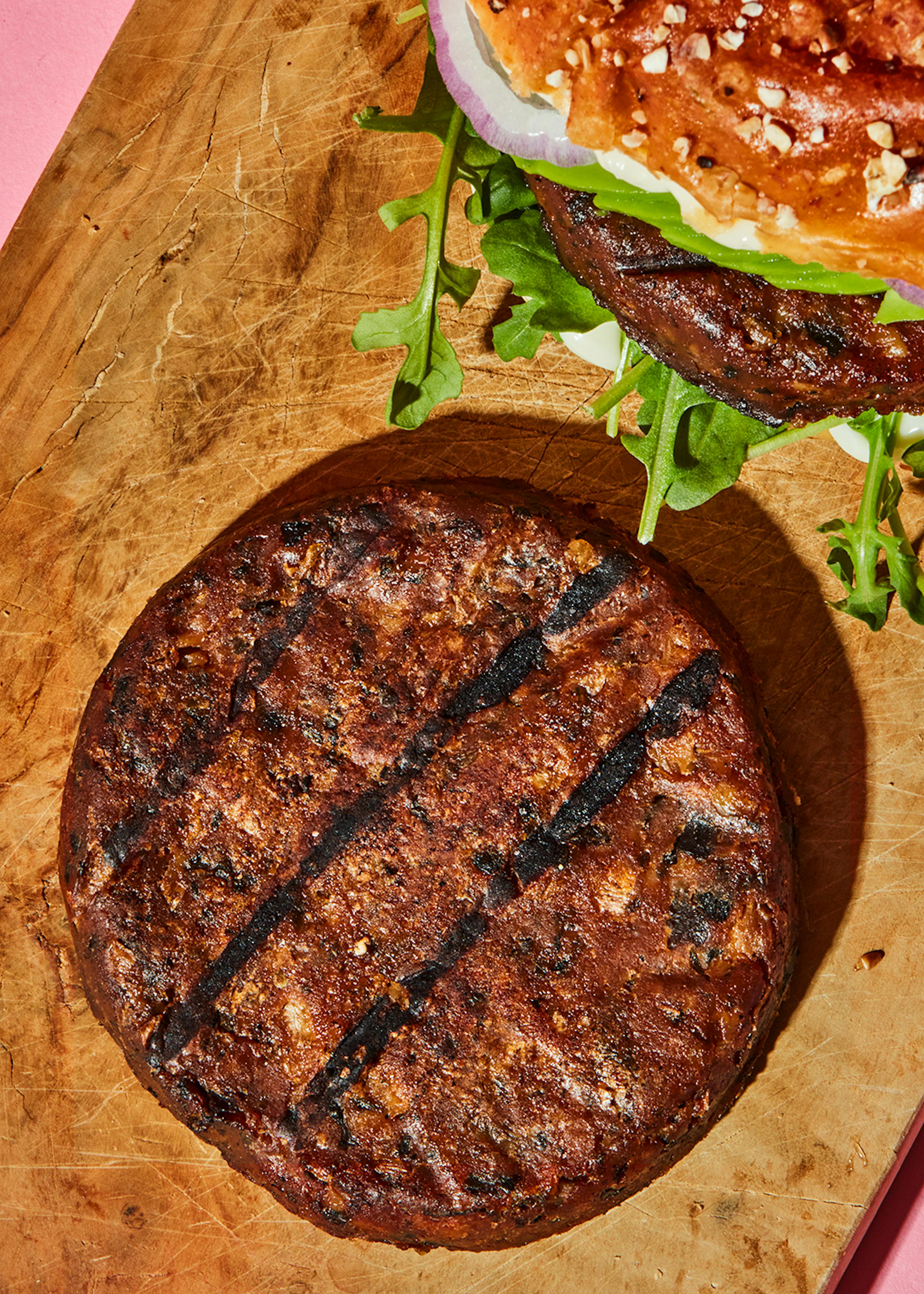 ein Stück Fleisch liegt auf einem Schneidebrett neben einem Sandwich