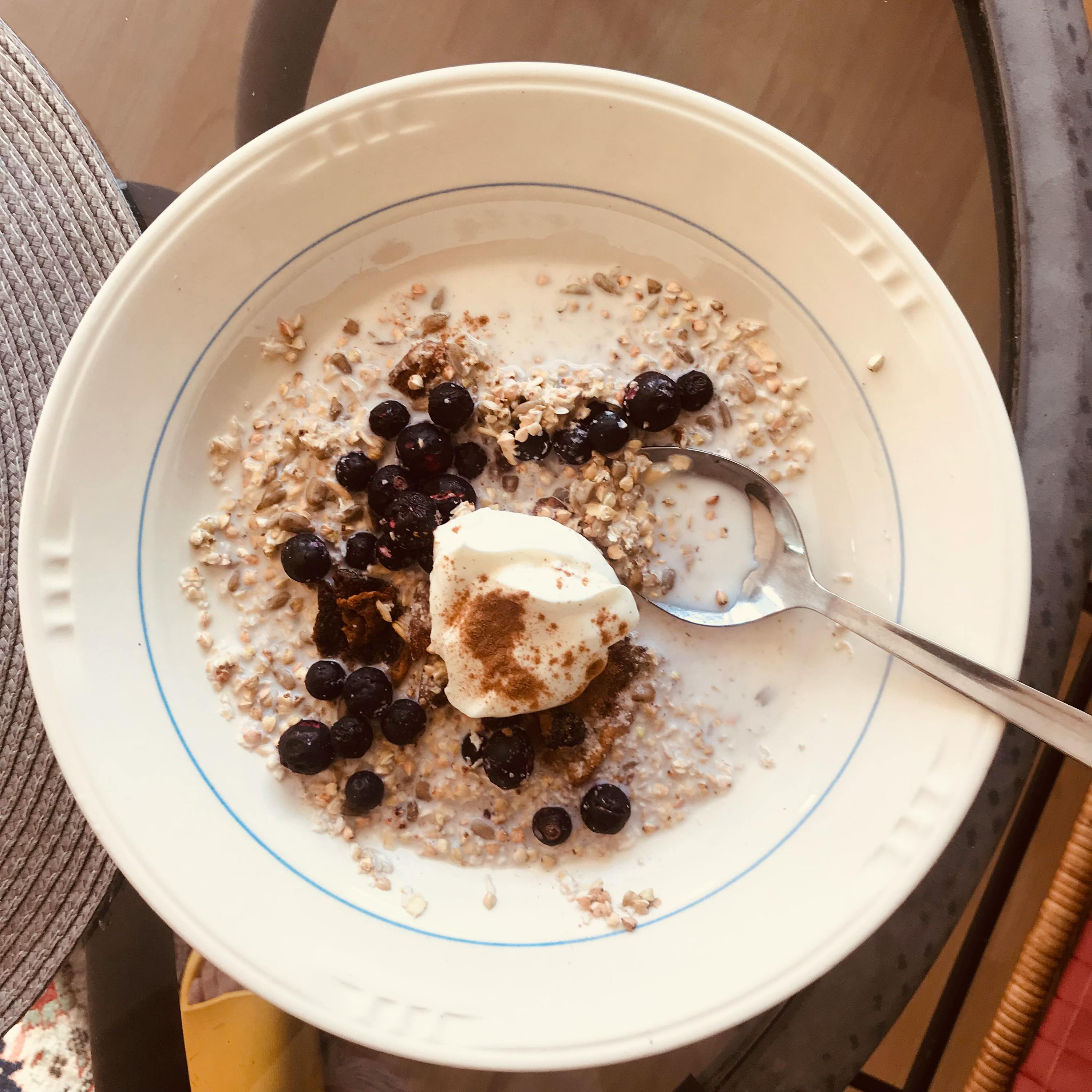 eine Schüssel Haferflocken mit Blaubeeren und Schlagsahne mit einem Löffel darin