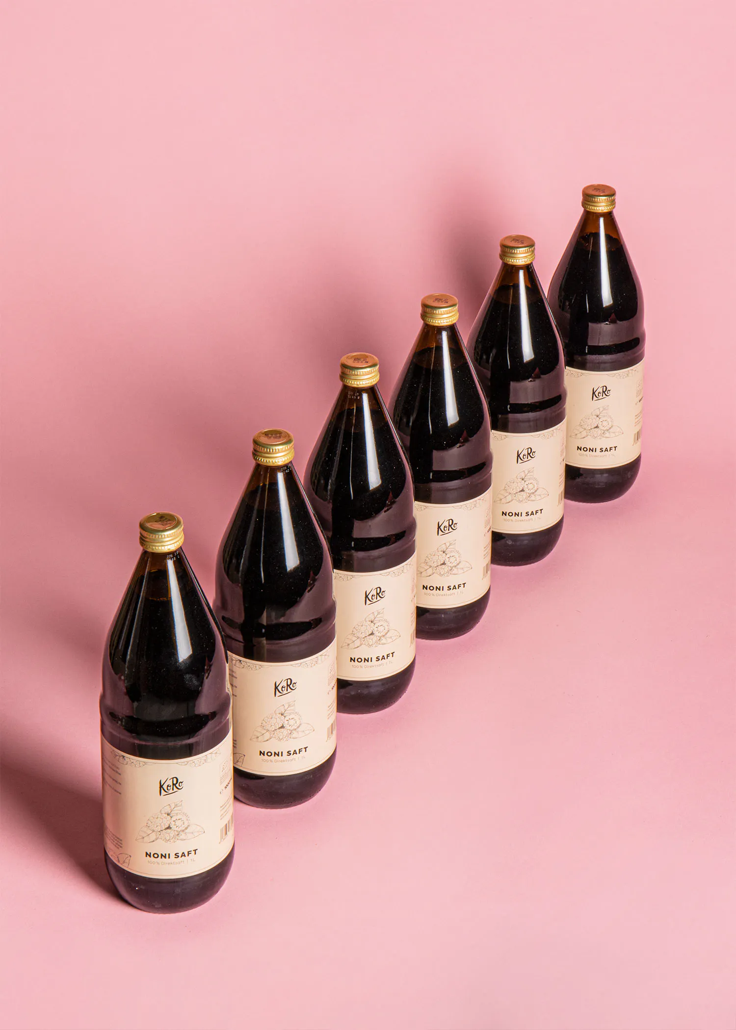 six bouteilles de noni saff sont alignées sur un fond rose