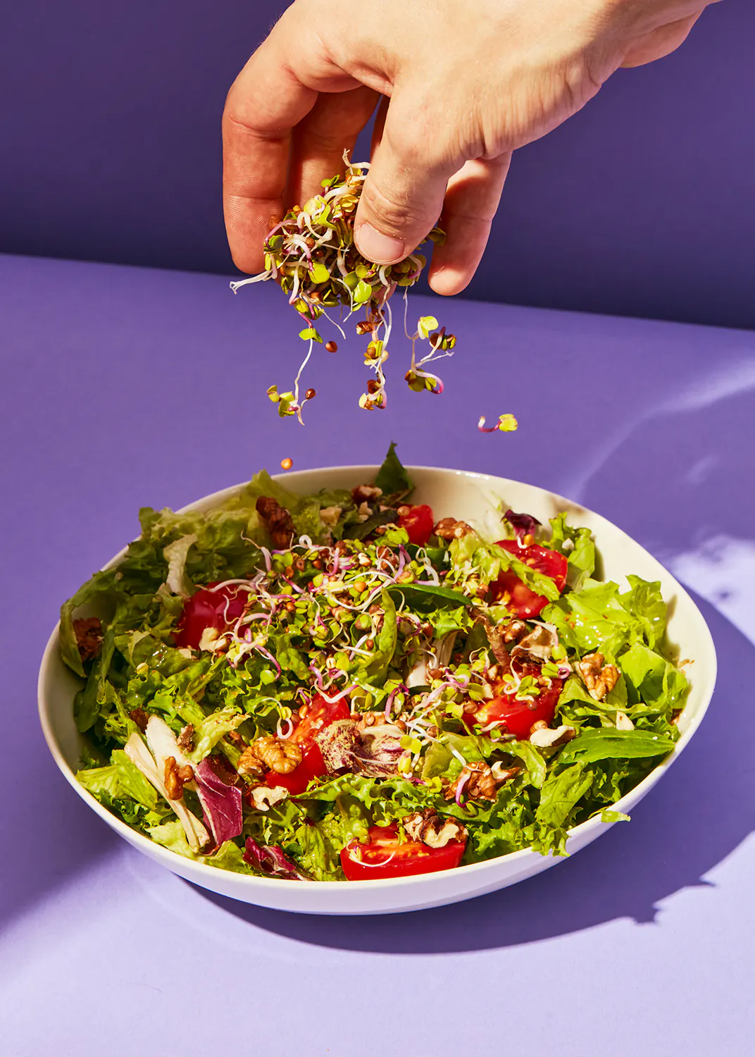 a person is pouring sprouts into a salad