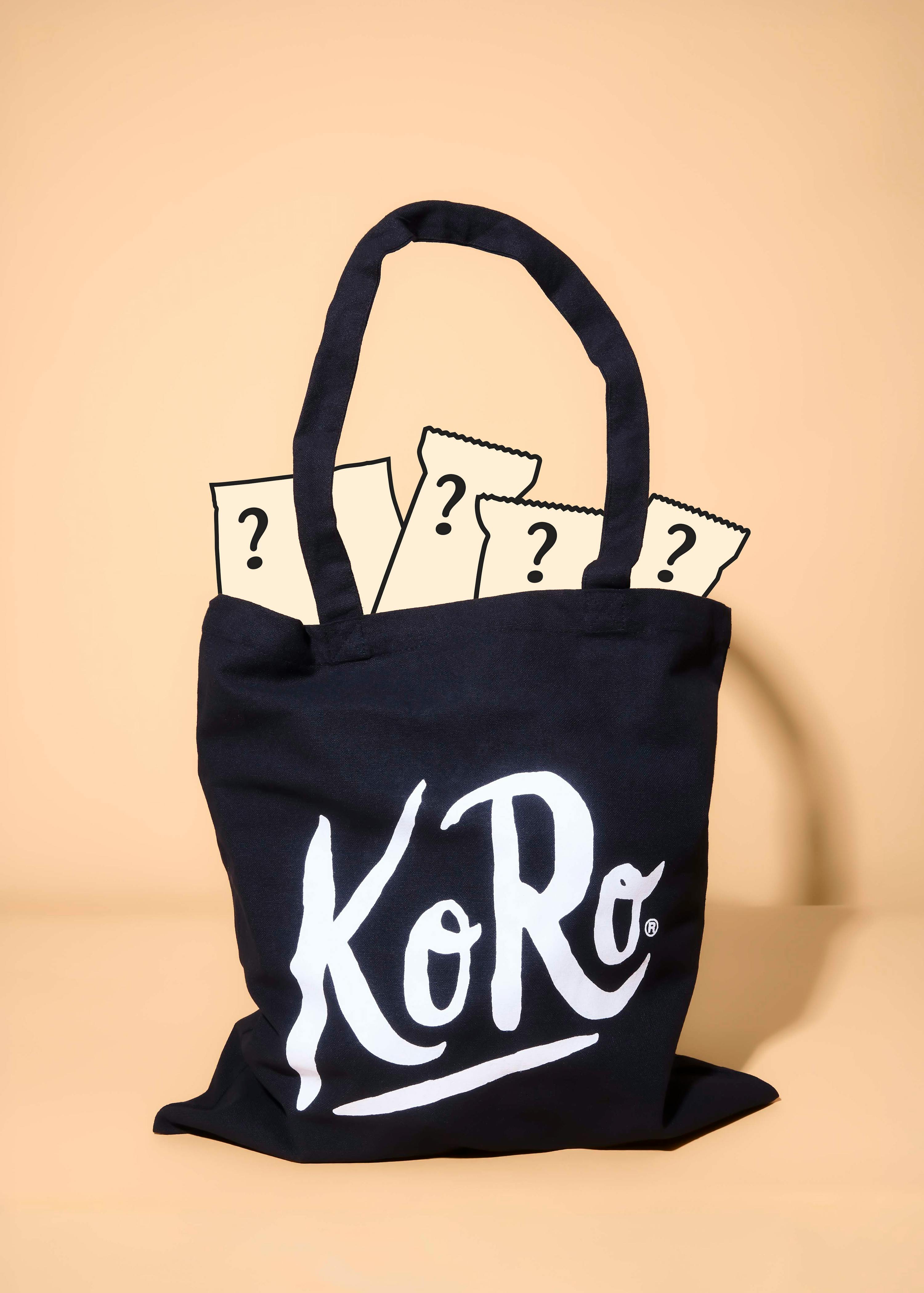 una borsa tote nera con il logo koro bianco, contenente diversi pacchetti misteriosi con punti interrogativi.