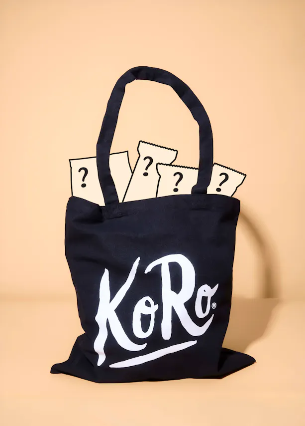 a black koro tote bag filled with several mystery packages featuring question marks.