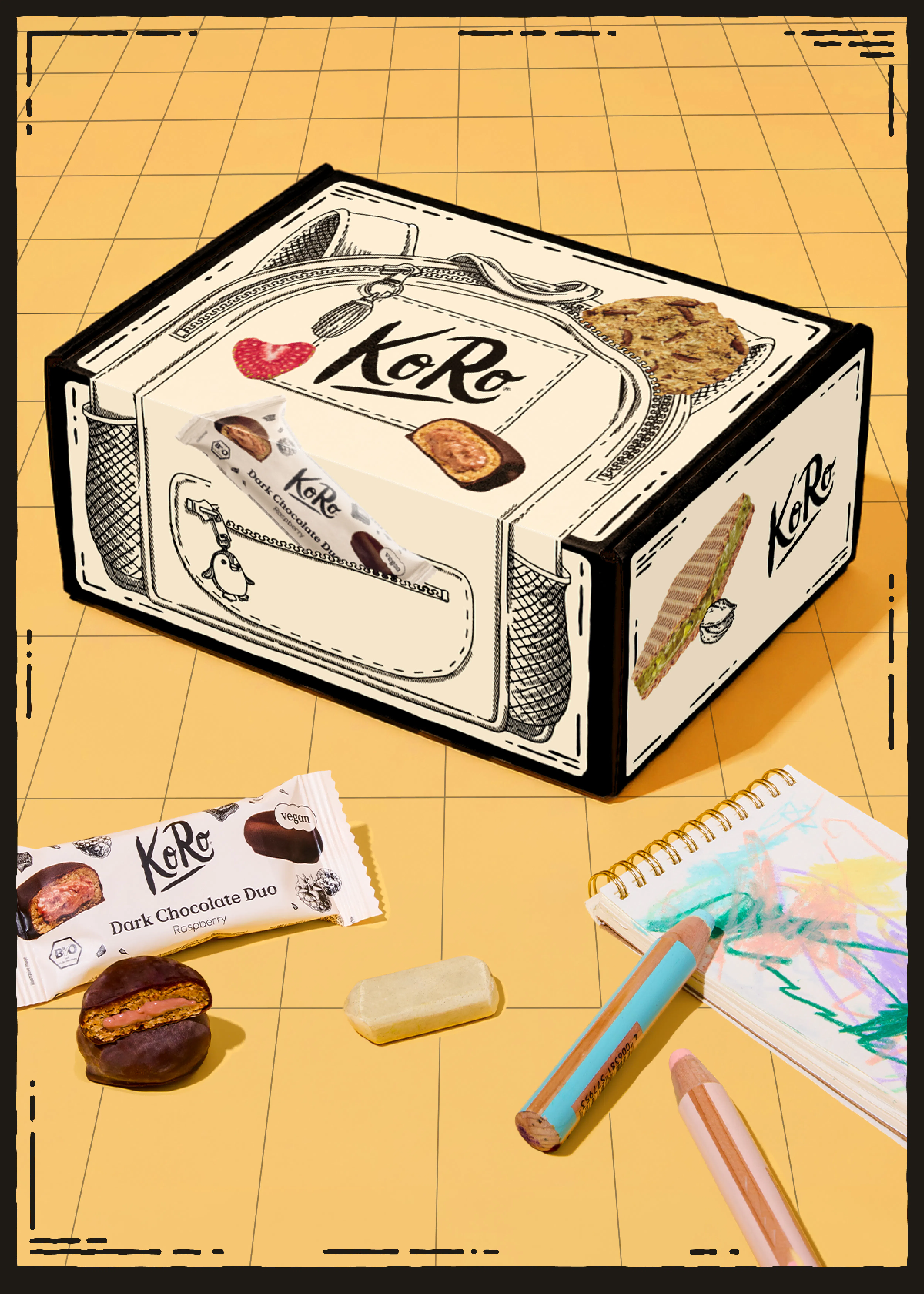 eine koro-geschenkbox mit illustrationen von snacks, daneben liegen ein riegel, ein halbierter schokoriegel, ein radiergummi und buntstifte auf einem gelben hintergrund.