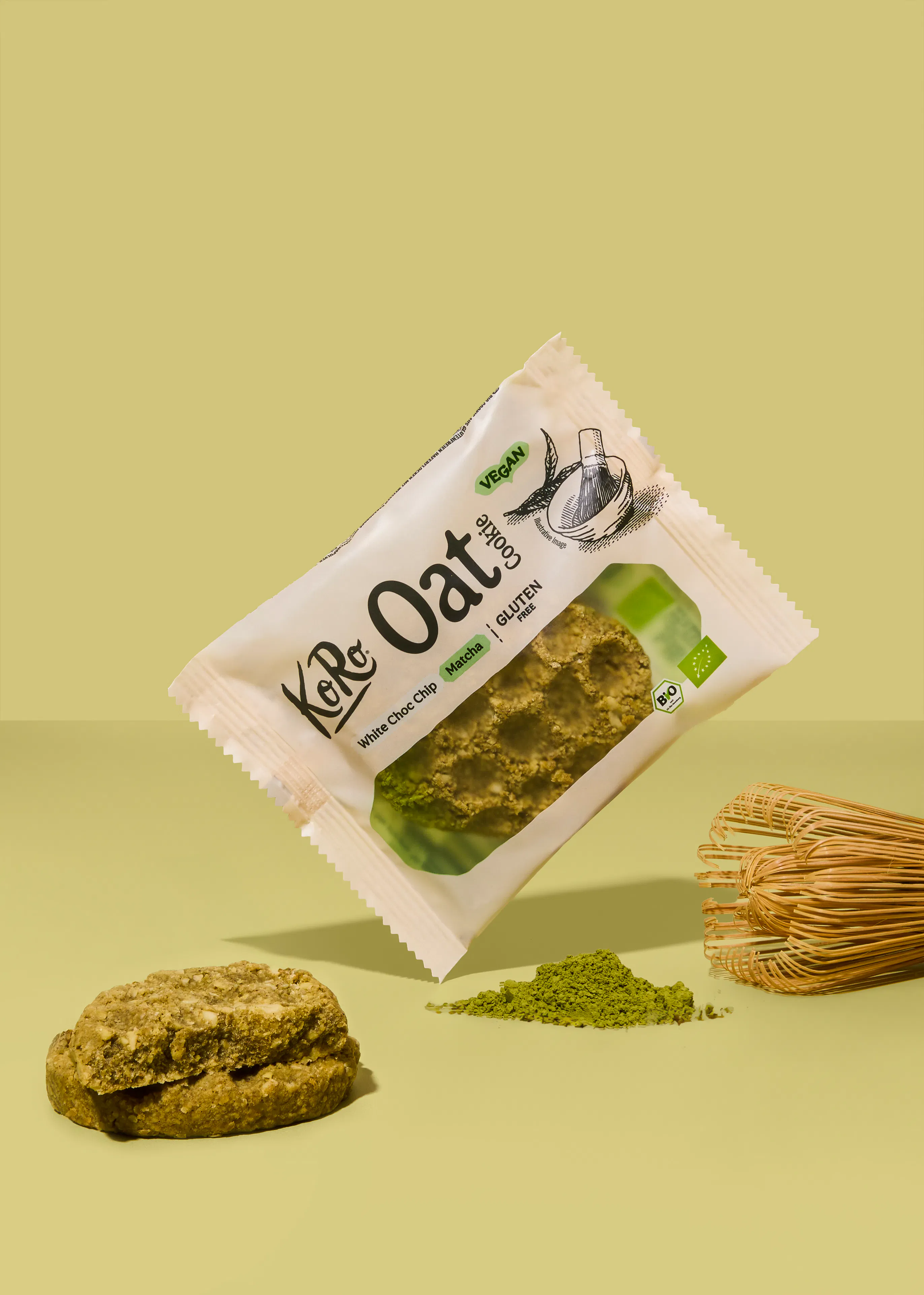 eine verpackung eines koro oat cookies mit matcha und white choc chip geschmack schwebt neben einem bambusbesen und einem matcha-keks auf einem hellgrünen hintergrund.
