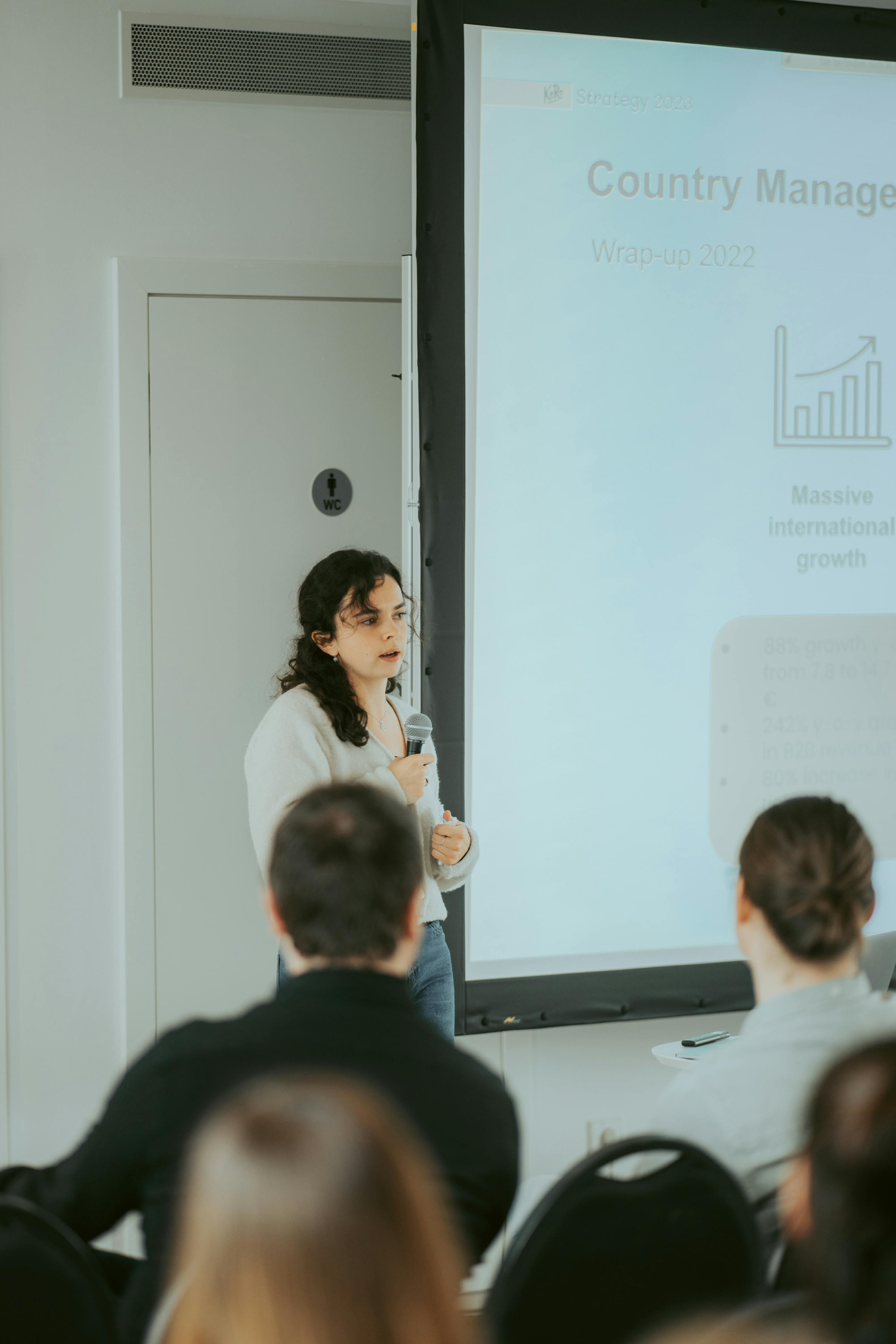 una donna tiene in mano un microfono davanti a un proiettore che mostra il titolo " country manager "