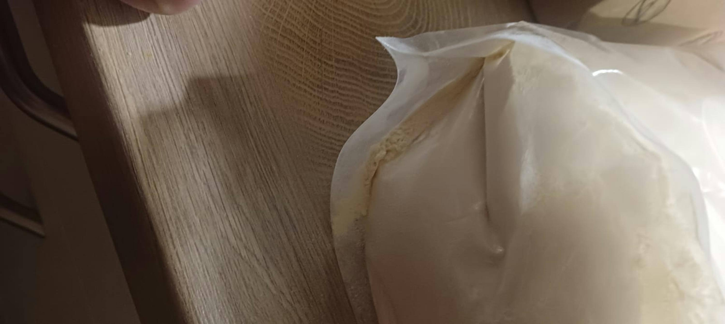 un sac en plastique transparent ouvert contenant une substance granuleuse claire, posé sur une surface en bois.