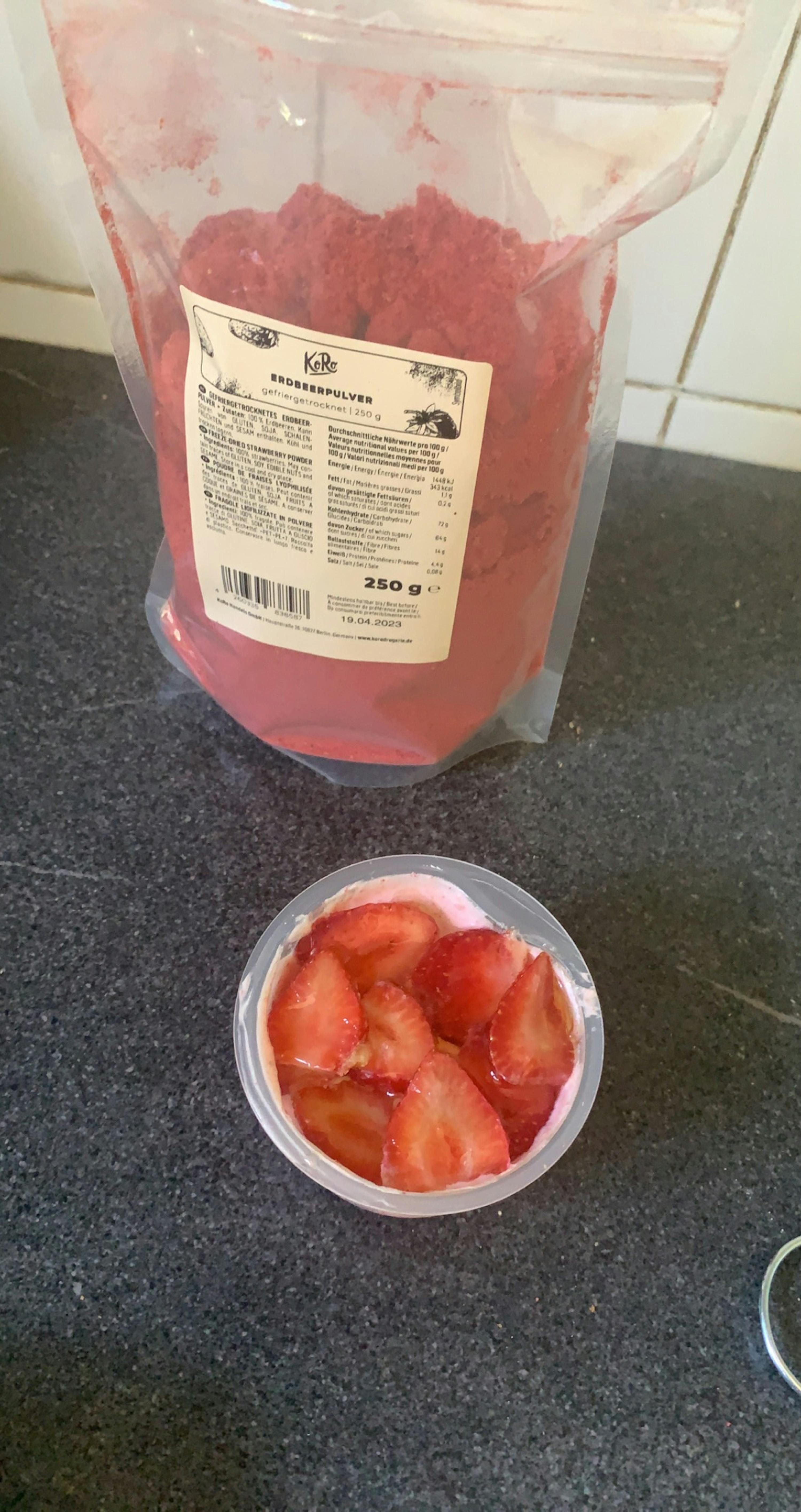 ein Plastikbecher mit Erdbeeren neben einem Plastikbeutel mit Erdbeerpulver