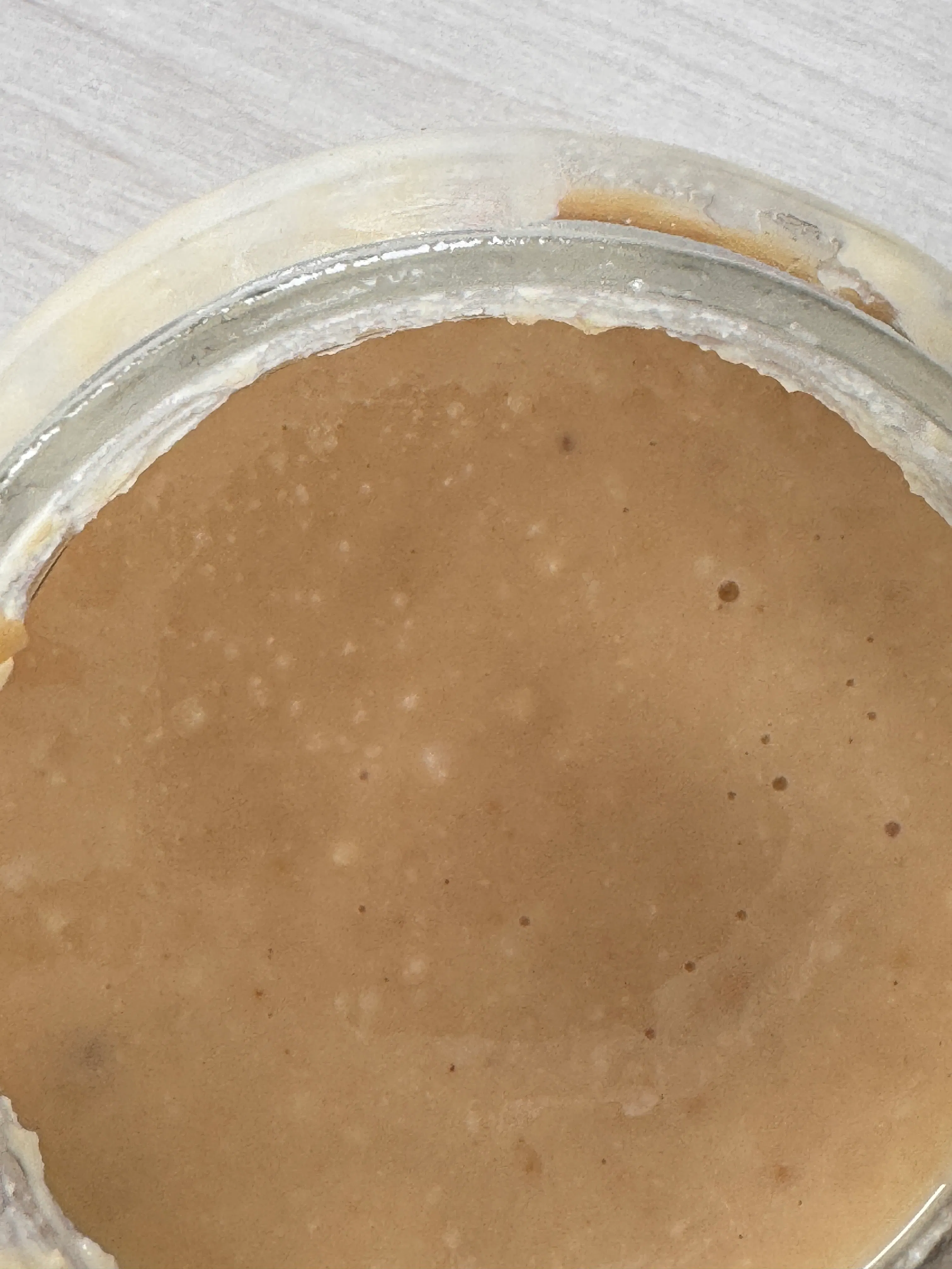 nahaufnahme einer hellbraunen, blasenhaltigen flüssigkeit in einem glasgefäß, möglicherweise ein sauerteigstarter.