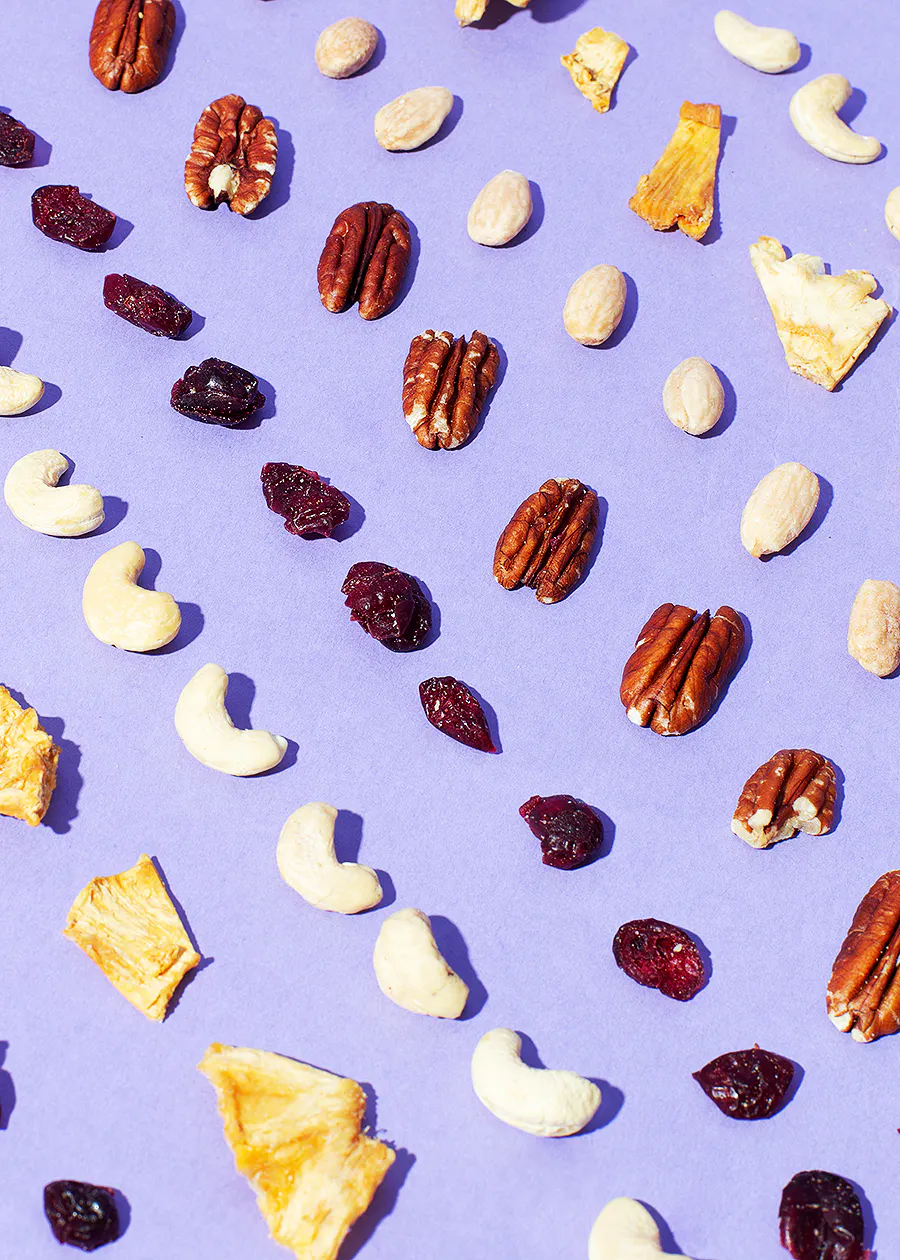 verschiedene Nüsse und Trockenfrüchte auf einem lila Hintergrund