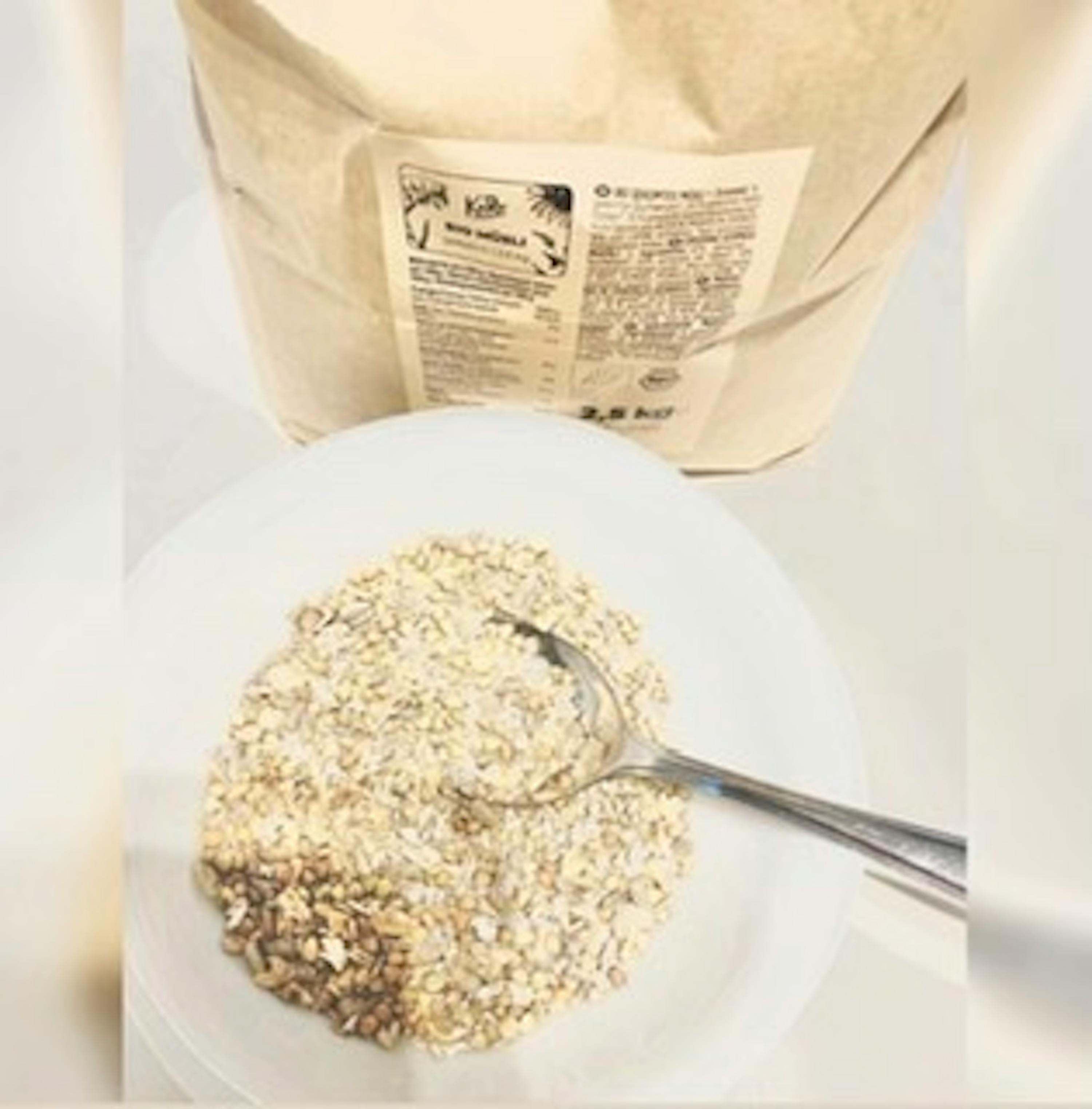 ein weißer Teller mit Haferflocken und einem Löffel neben einer Tüte Haferflocken