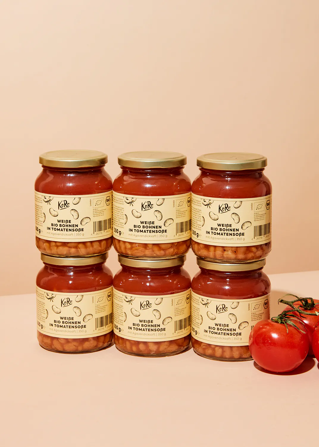 sechs Gläser weiße Bohnen in Tomatensauce stehen neben einer Tomate