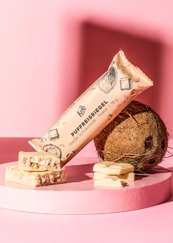 une barre de chocolat blanc est posée sur une table rose à côté d' une noix de coco