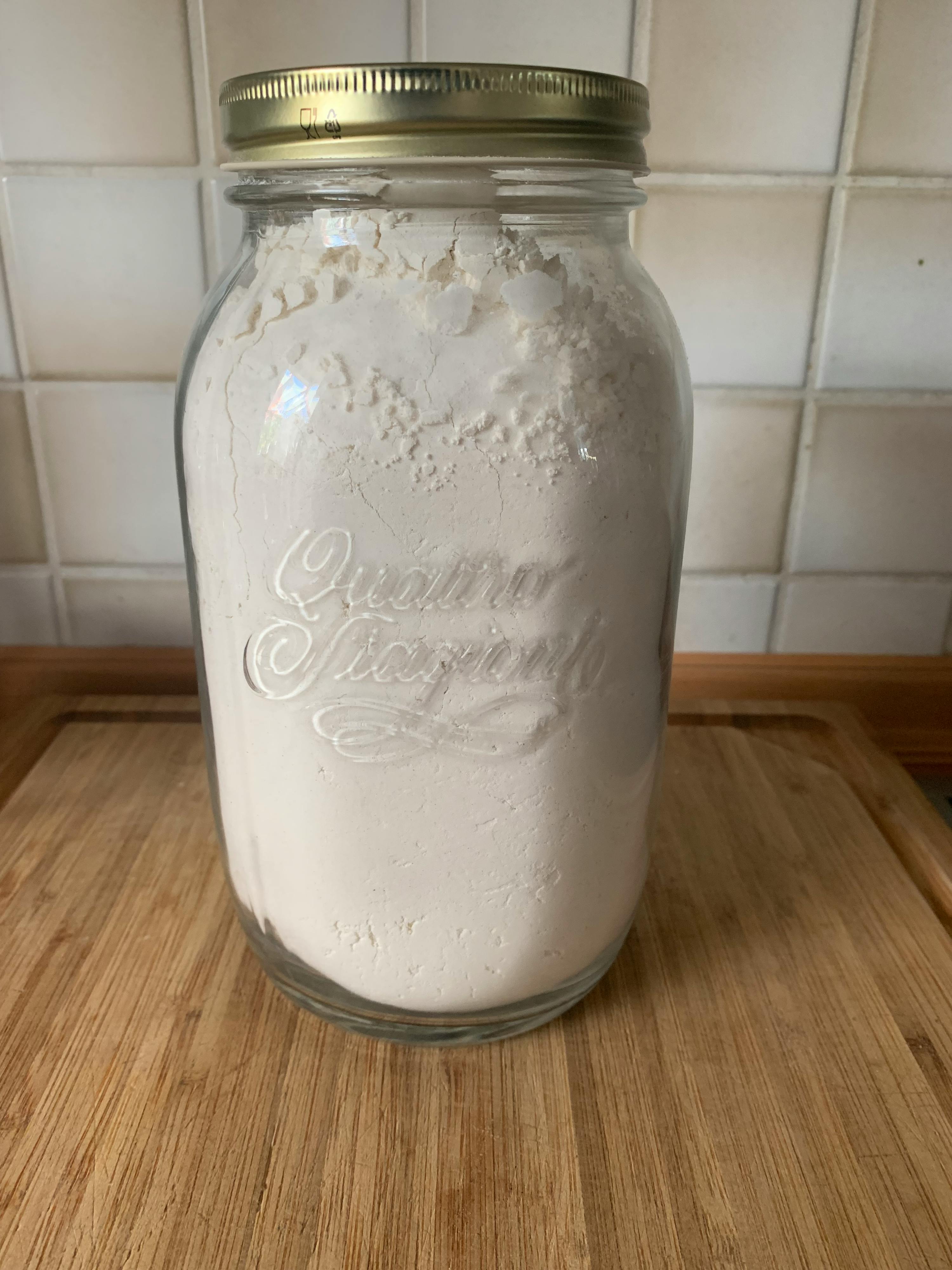 un barattolo di vetro pieno di farina si trova su un tagliere di legno