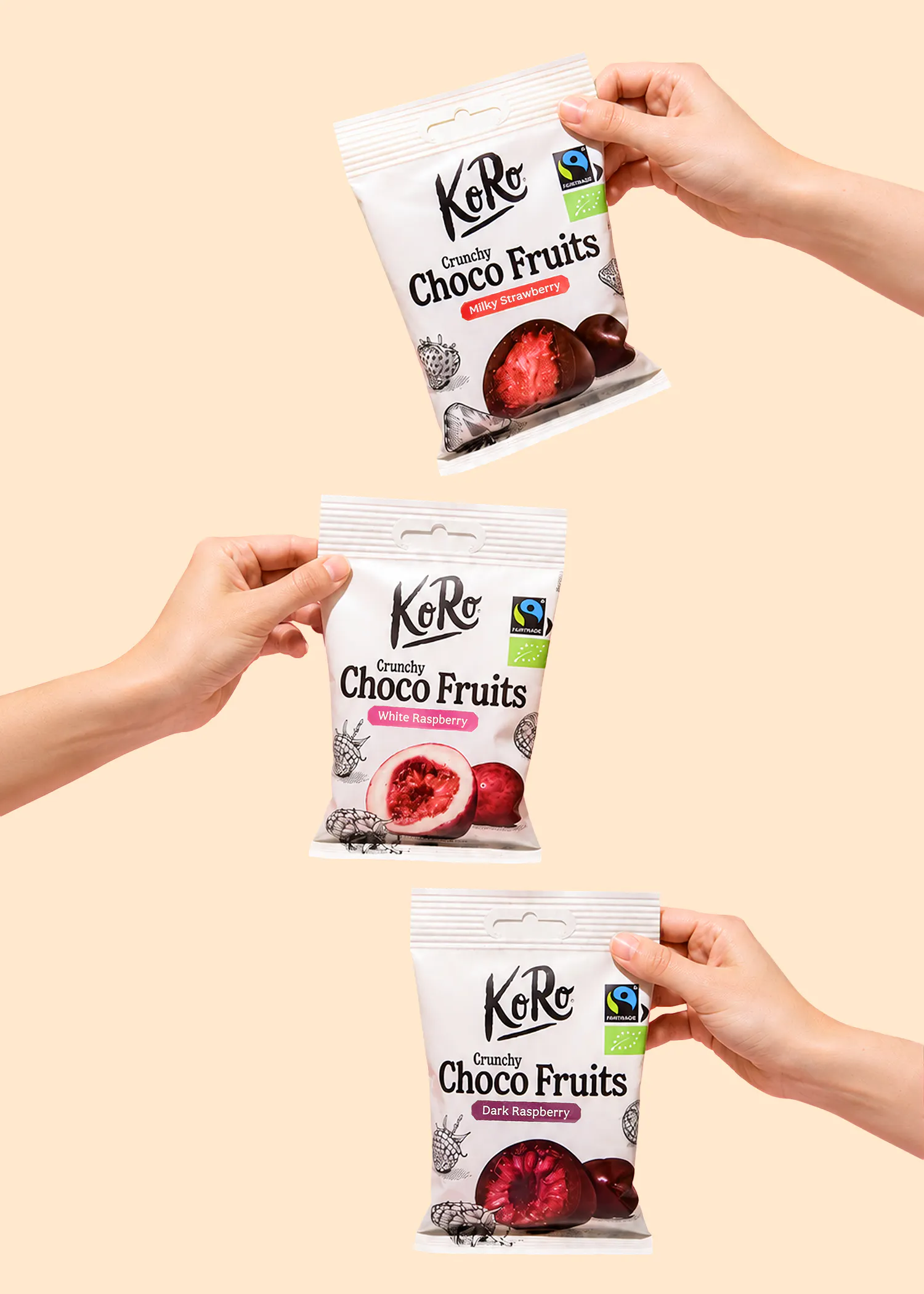 trois mains tiennent trois sachets de koro crunchy choco fruits aux saveurs fraise lactée, framboise blanche et framboise noire.