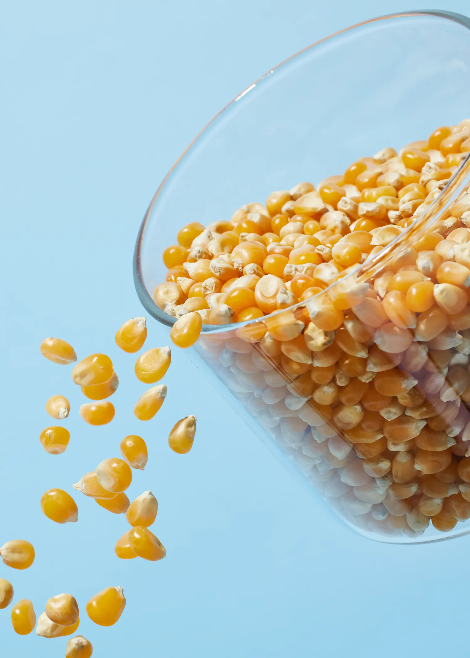 corn is being poured into a glass bowl on a blue background