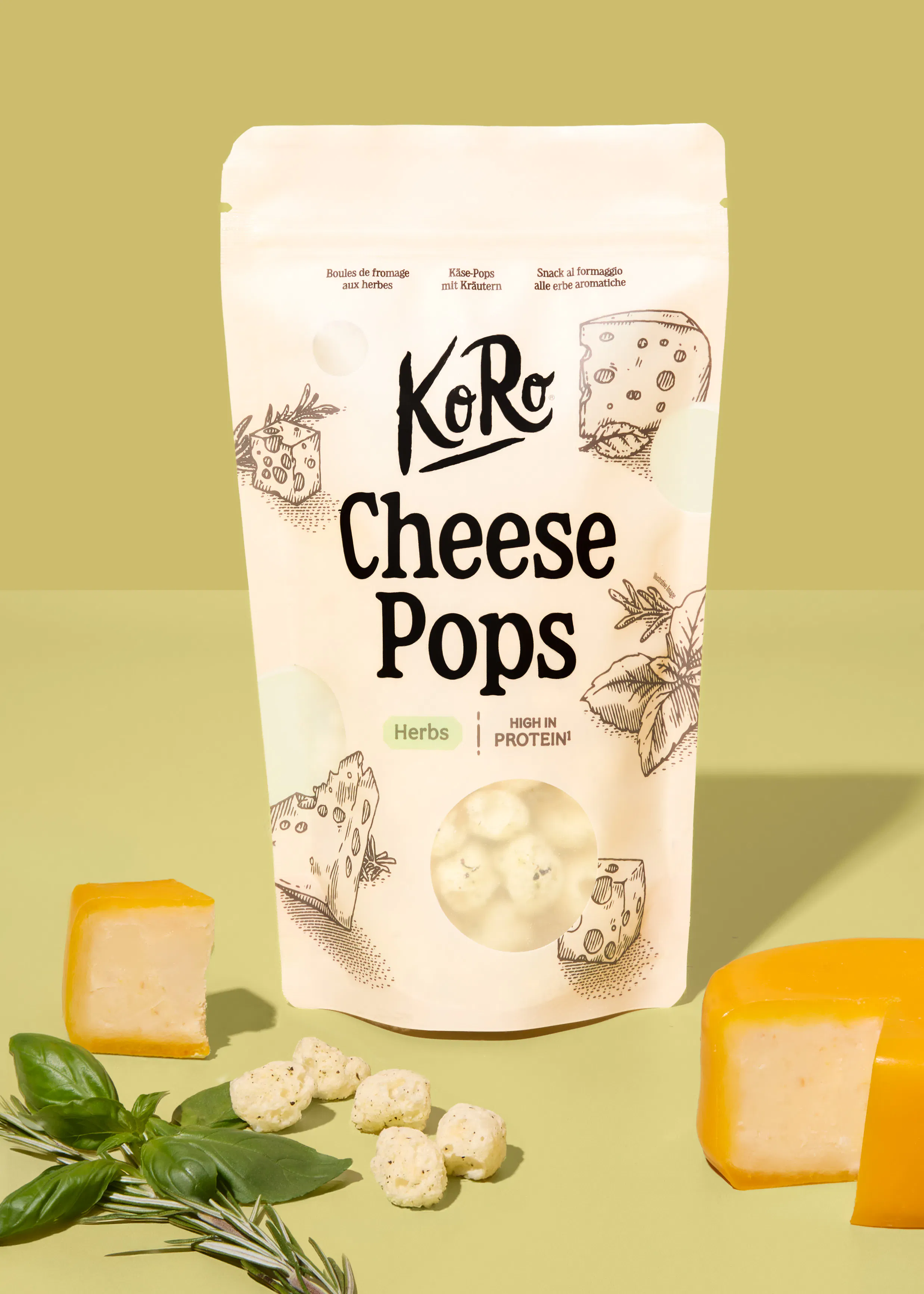 a bag of koro herb cheese pops sits on a light green surface surrounded by a block of cheese and fresh herbs.