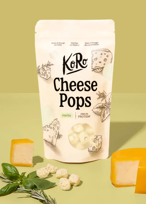 confezione di koro cheese pops alle erbe aromatiche circondata da pezzi di formaggio e rametti di erbe fresche.