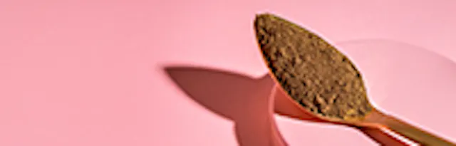 ein löffel mit braunem pulver liegt auf einem rosa hintergrund mit einem schatten.