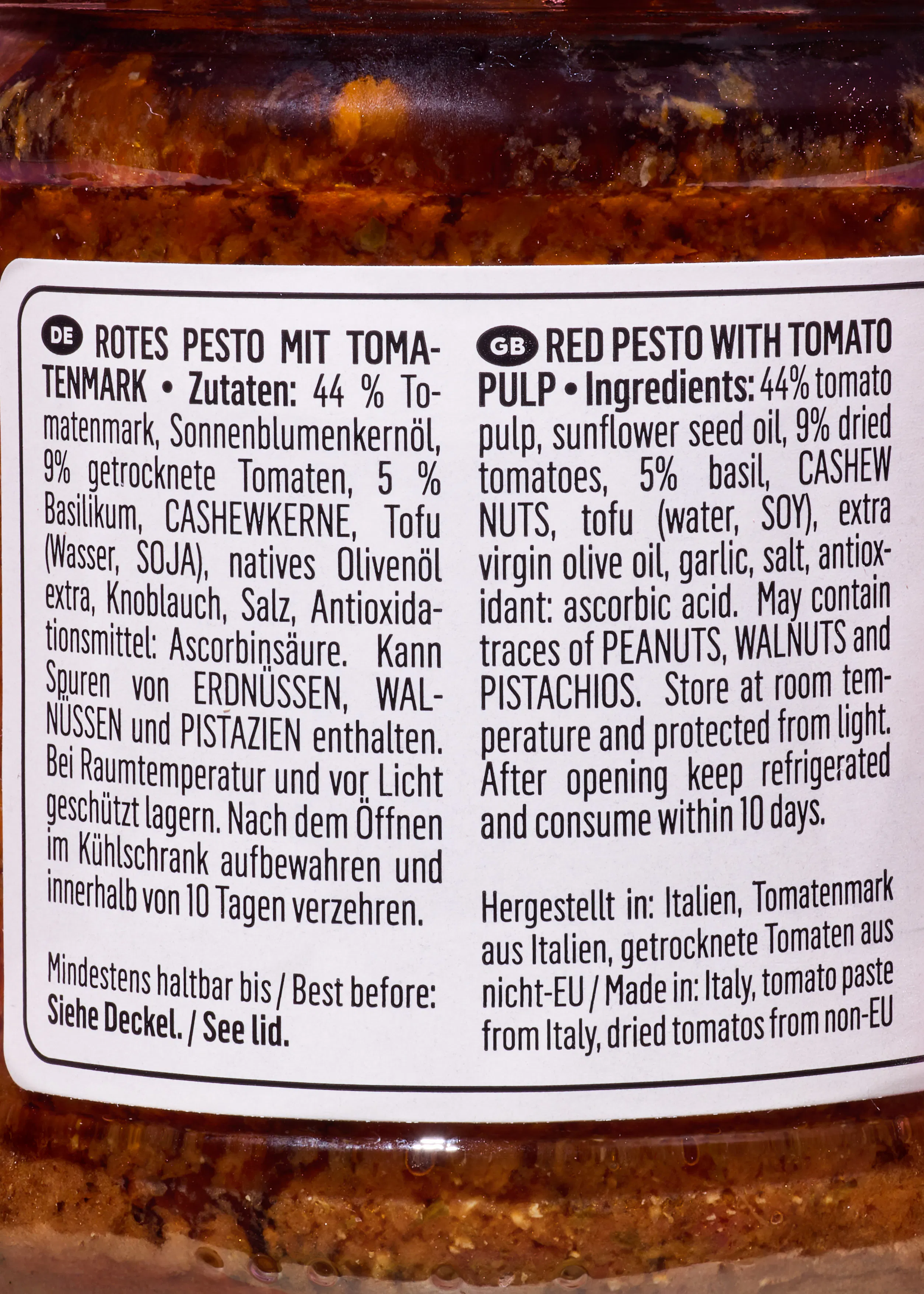 étiquette d'un pot de pesto rouge avec la liste des ingrédients et les instructions de conservation en allemand et en anglais.