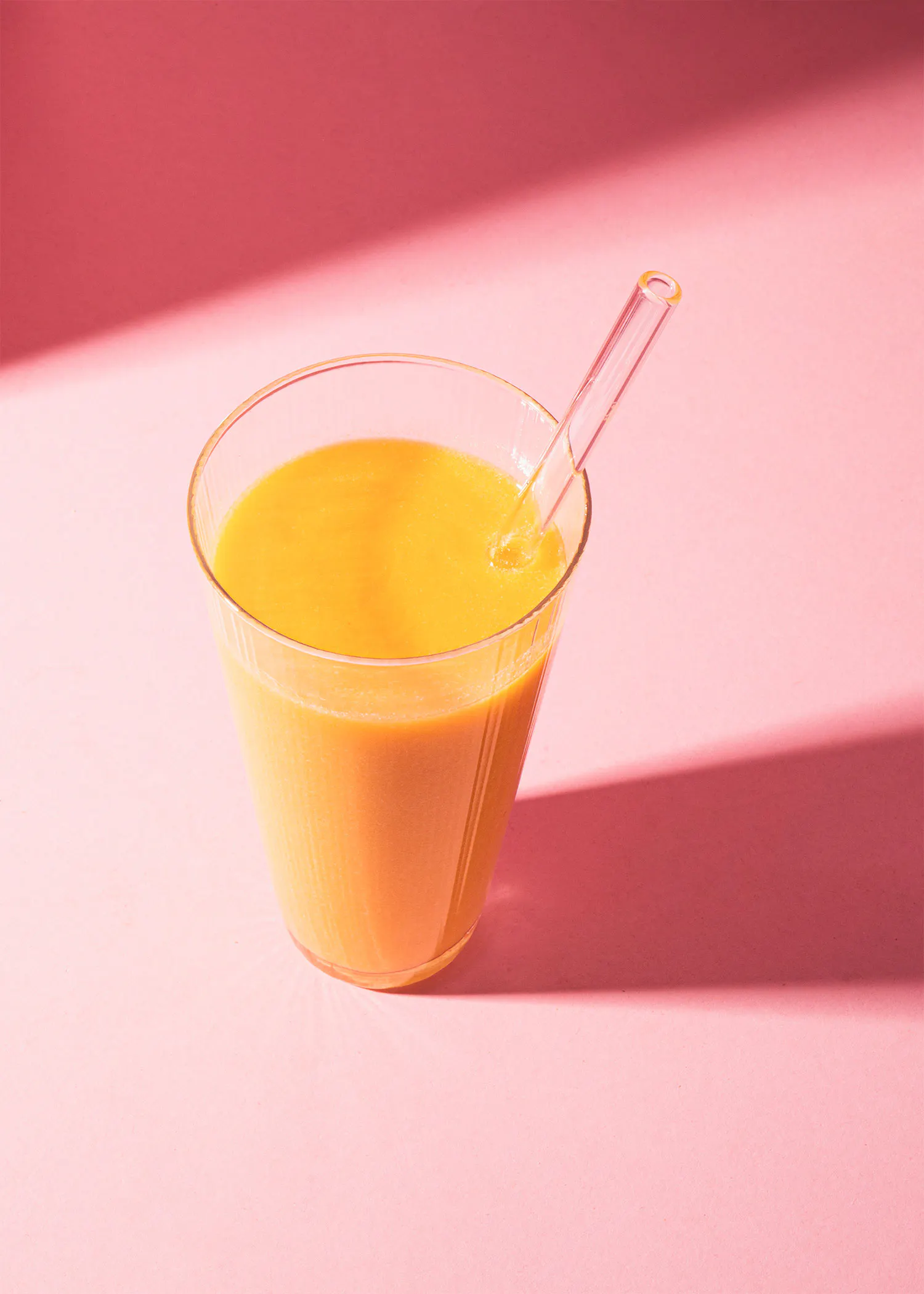 un verre de jus d' orange avec une paille sur un fond rose
