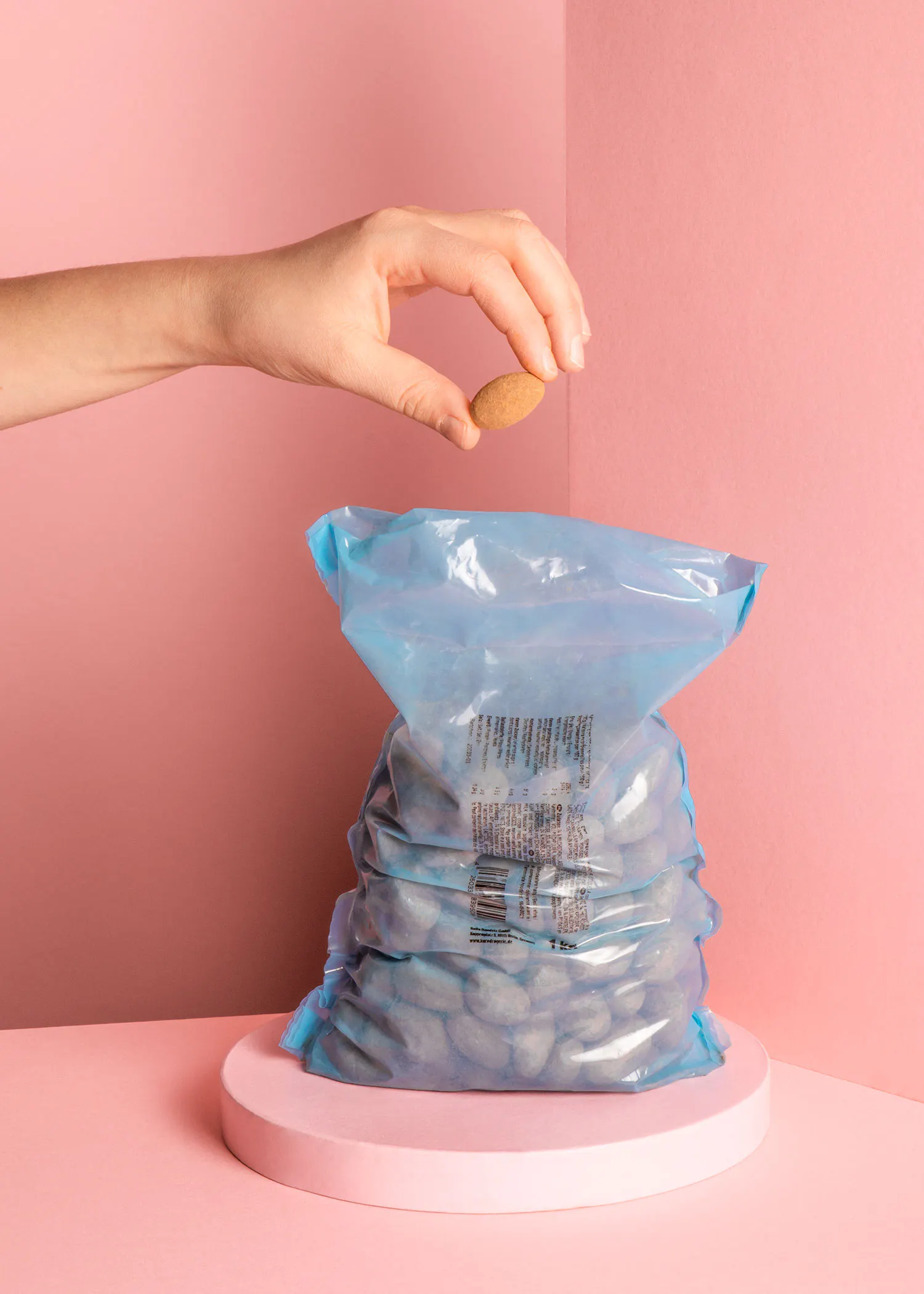 a hand is reaching into a bag of almonds on a pink surface