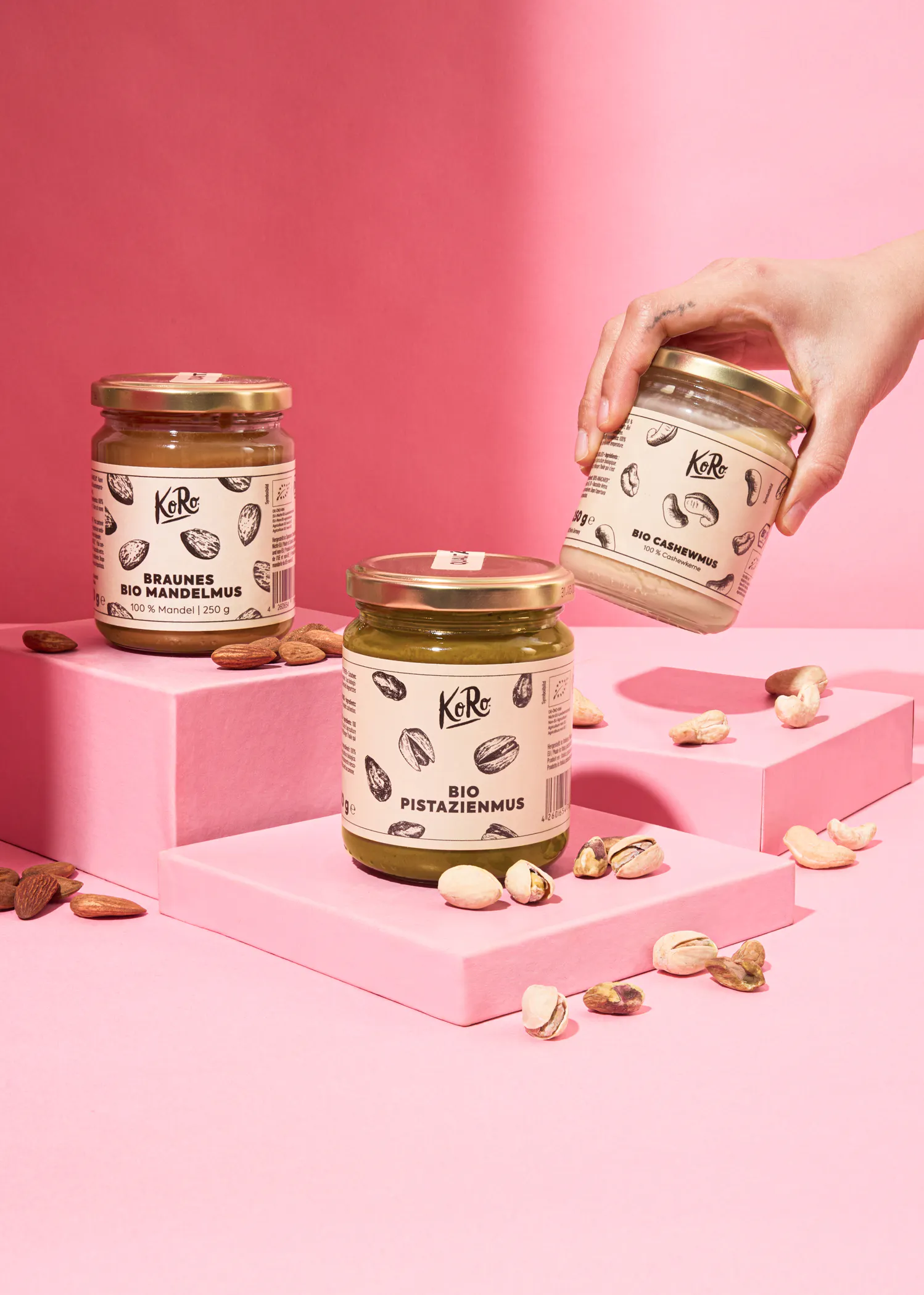 une personne tient un bocal de braune haselnus bio et un bocal de bio pistazienmus