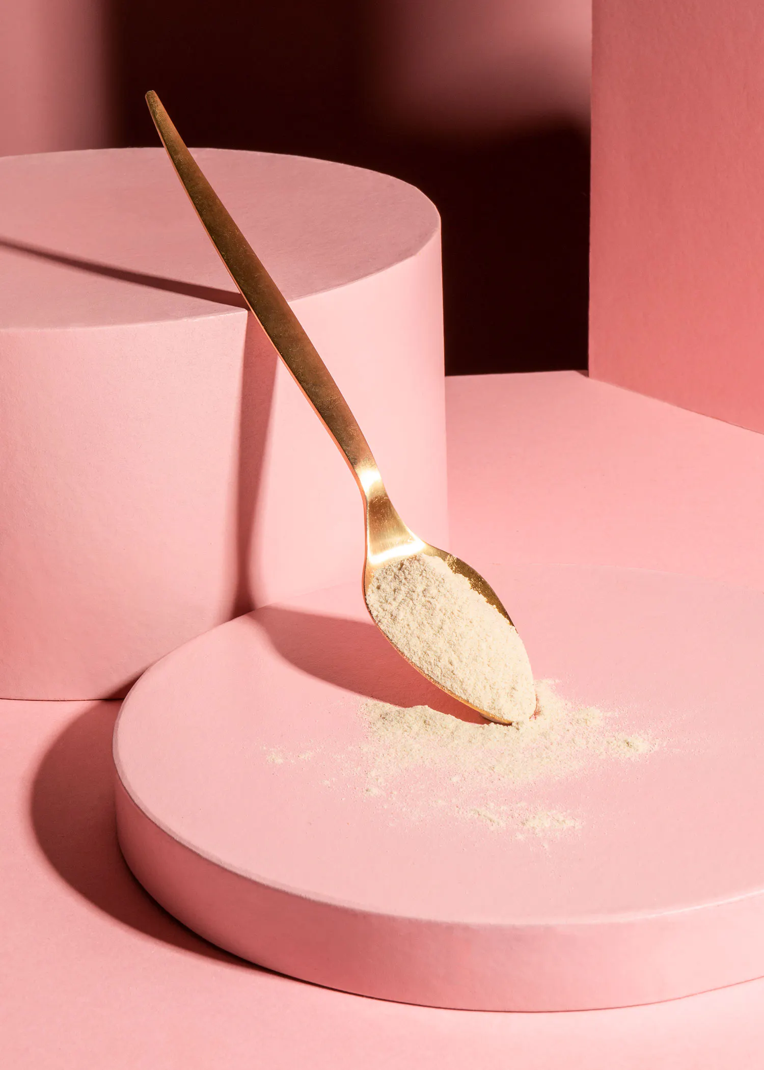 a gold spoon is filled with white powder on a pink surface