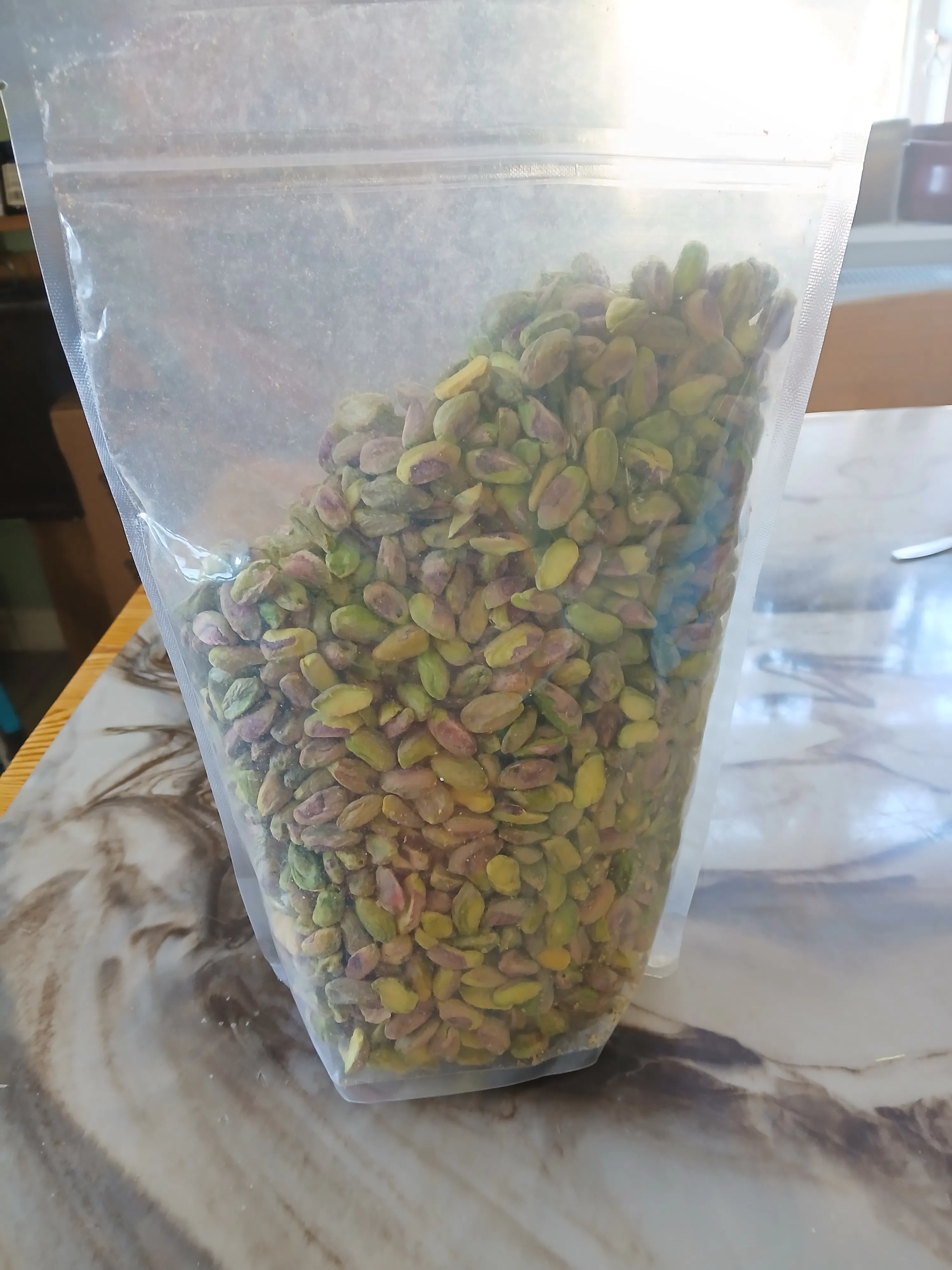 eine durchsichtige tüte gefüllt mit geschälten pistazien liegt auf einer marmorierten oberfläche.