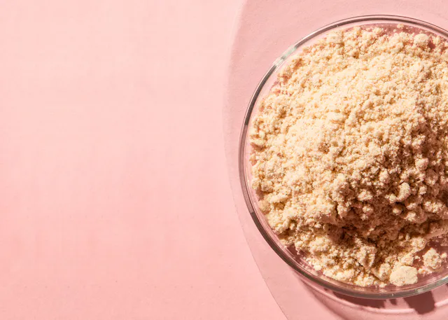 eine Glasschale mit braunem Pulver auf einem rosa Hintergrund