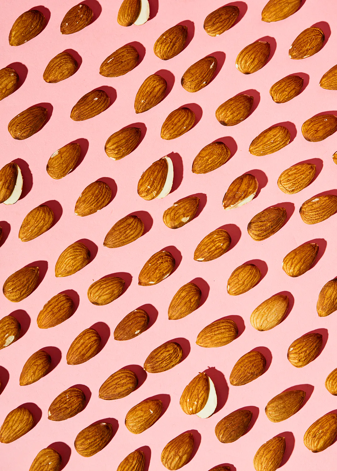 un motif d' amandes sur fond rose avec une amande coupée en deux