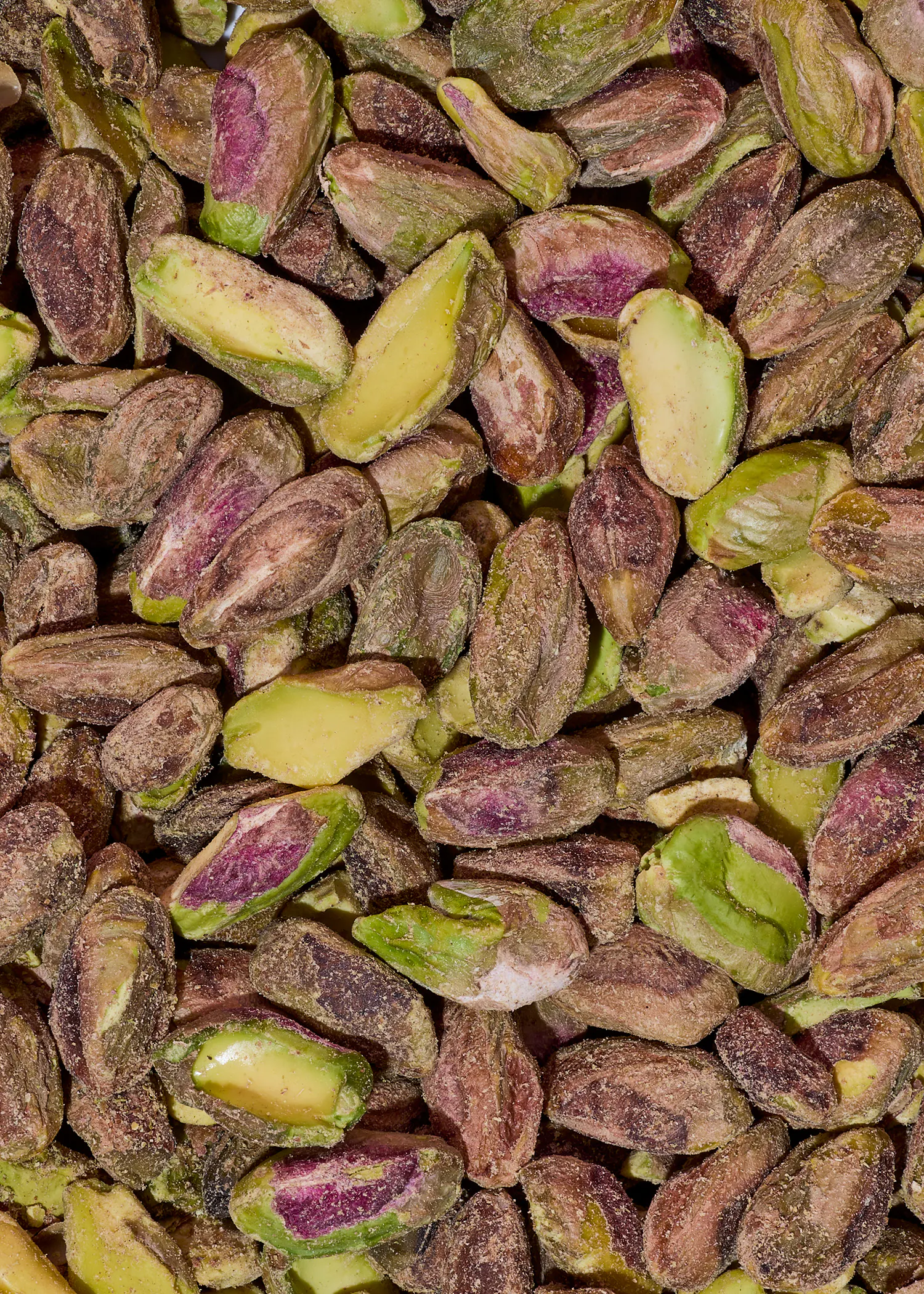 gros plan sur une multitude de pistaches décortiquées aux teintes vertes, violettes et jaunes.