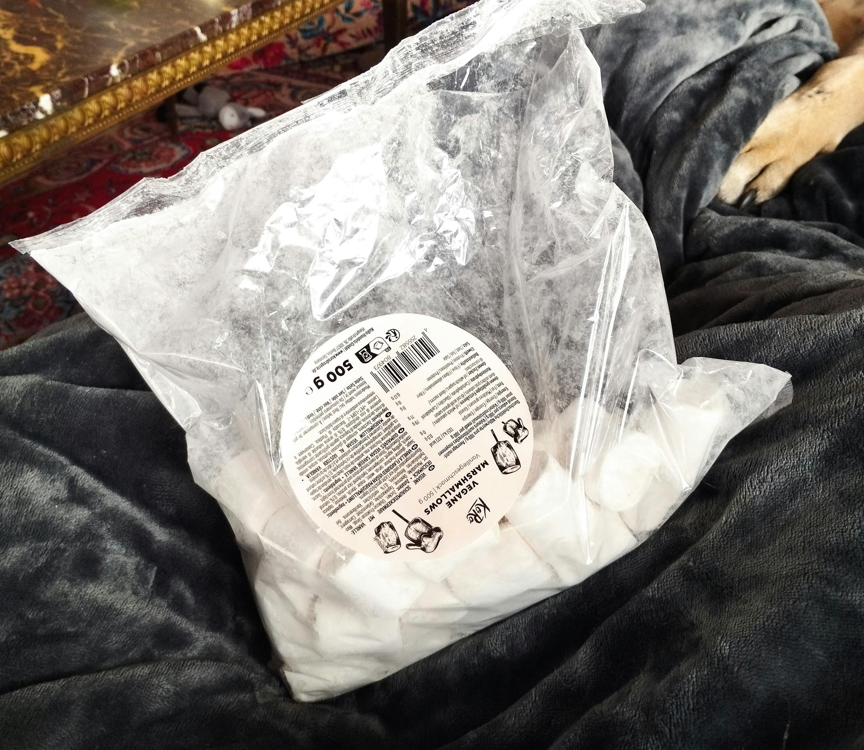 un sacchetto di marshmallows è seduto su un letto accanto a un cane