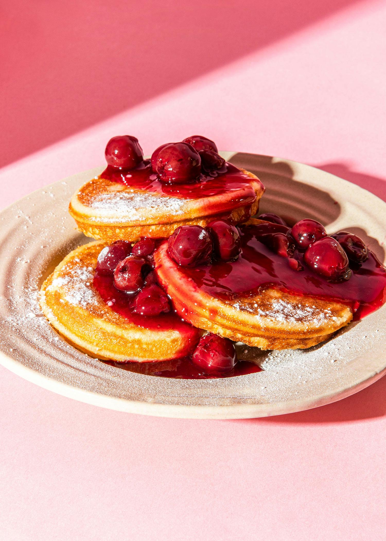 a plate of pancakes with cherries on top and powdered sugar