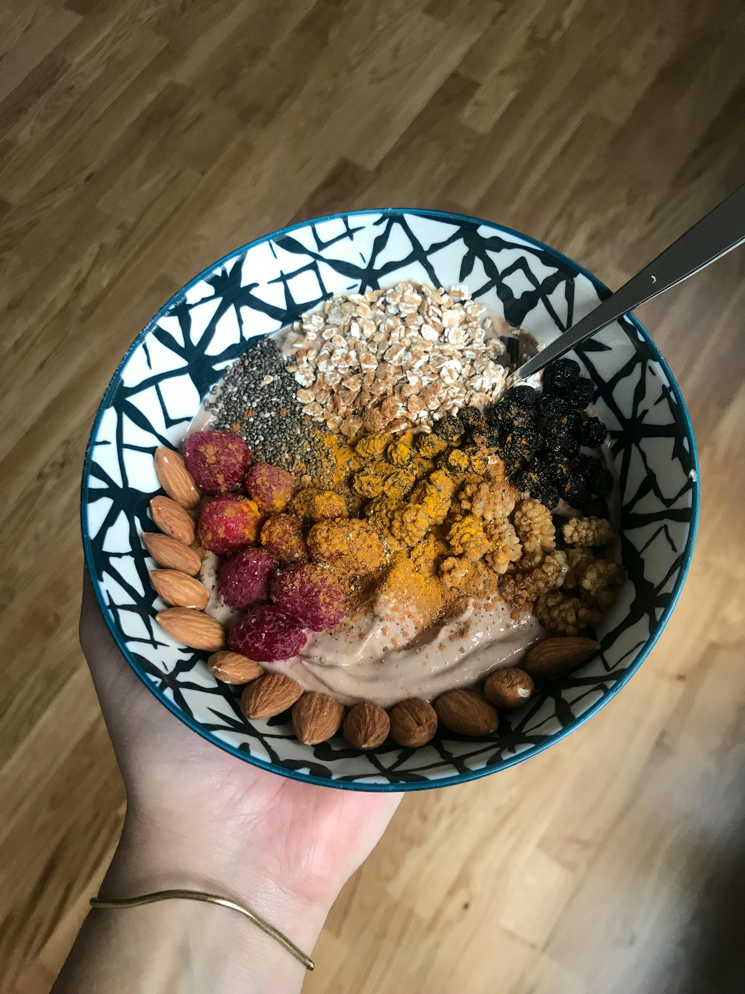 une personne tient un bol de céréales avec des noix et des framboises