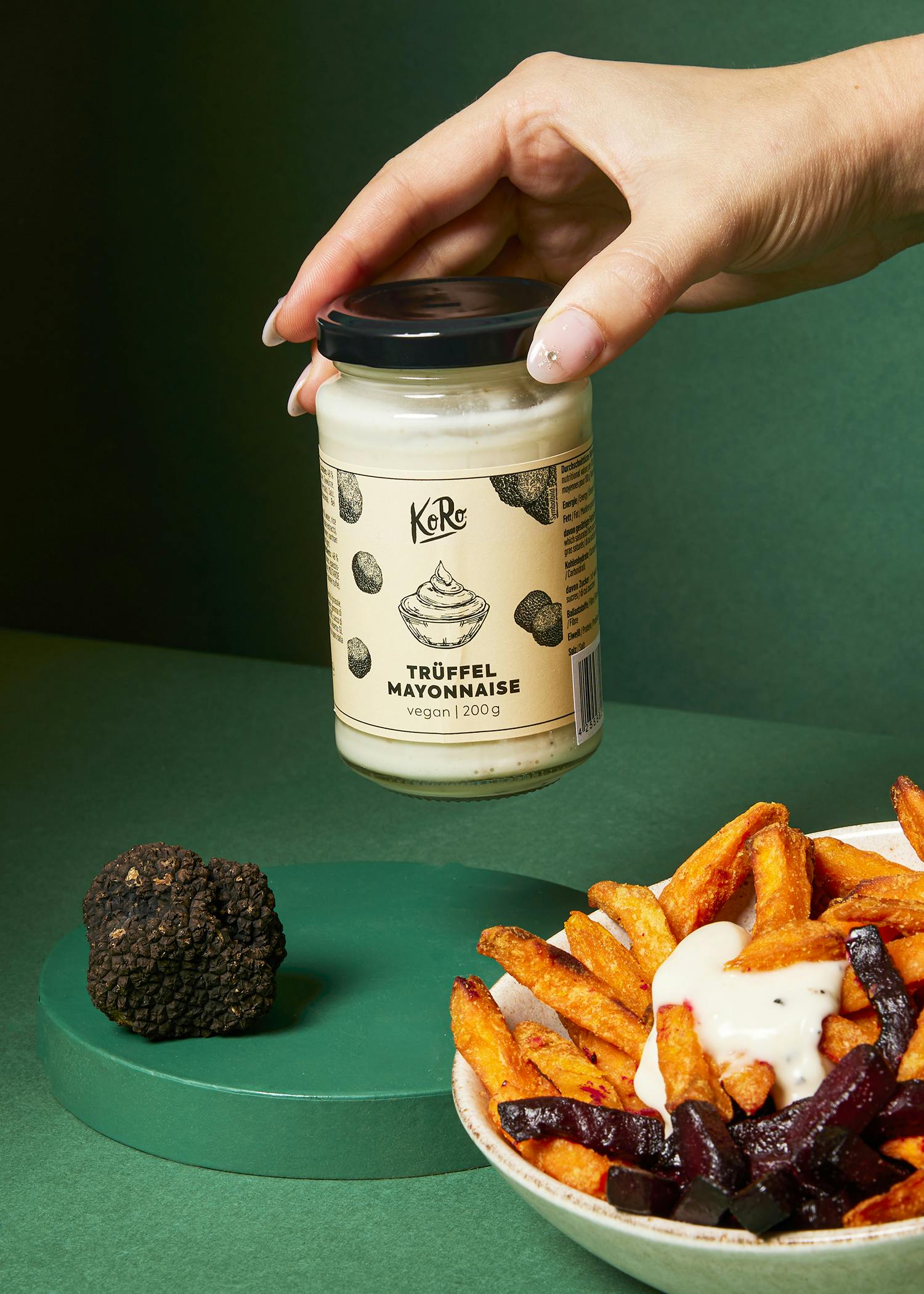 une main tient un pot de mayonnaise truffée à côté d' un bol de frites