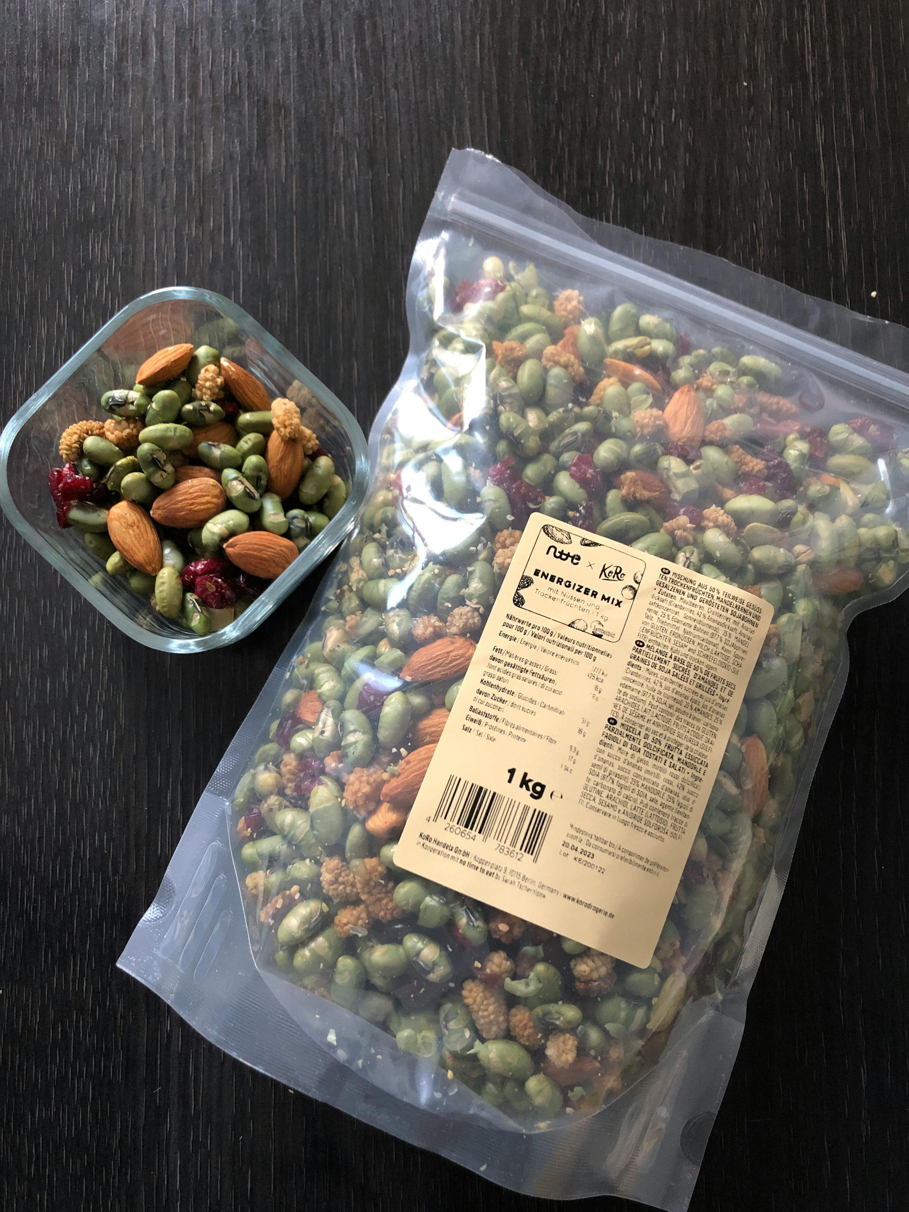 a bag of pumpkin seeds next to a glass container of nuts