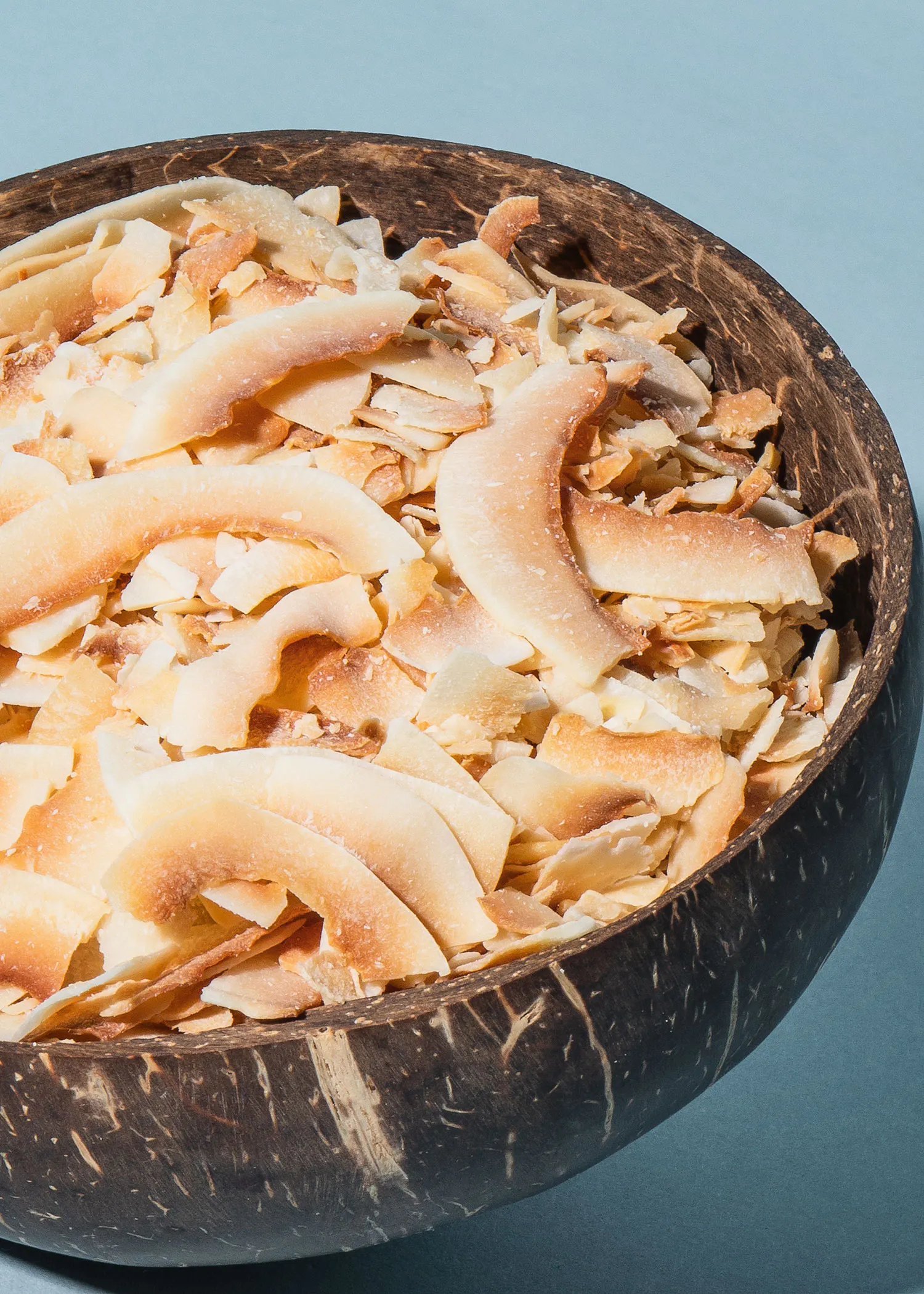 un bol en bois rempli de tranches de noix de coco séchées