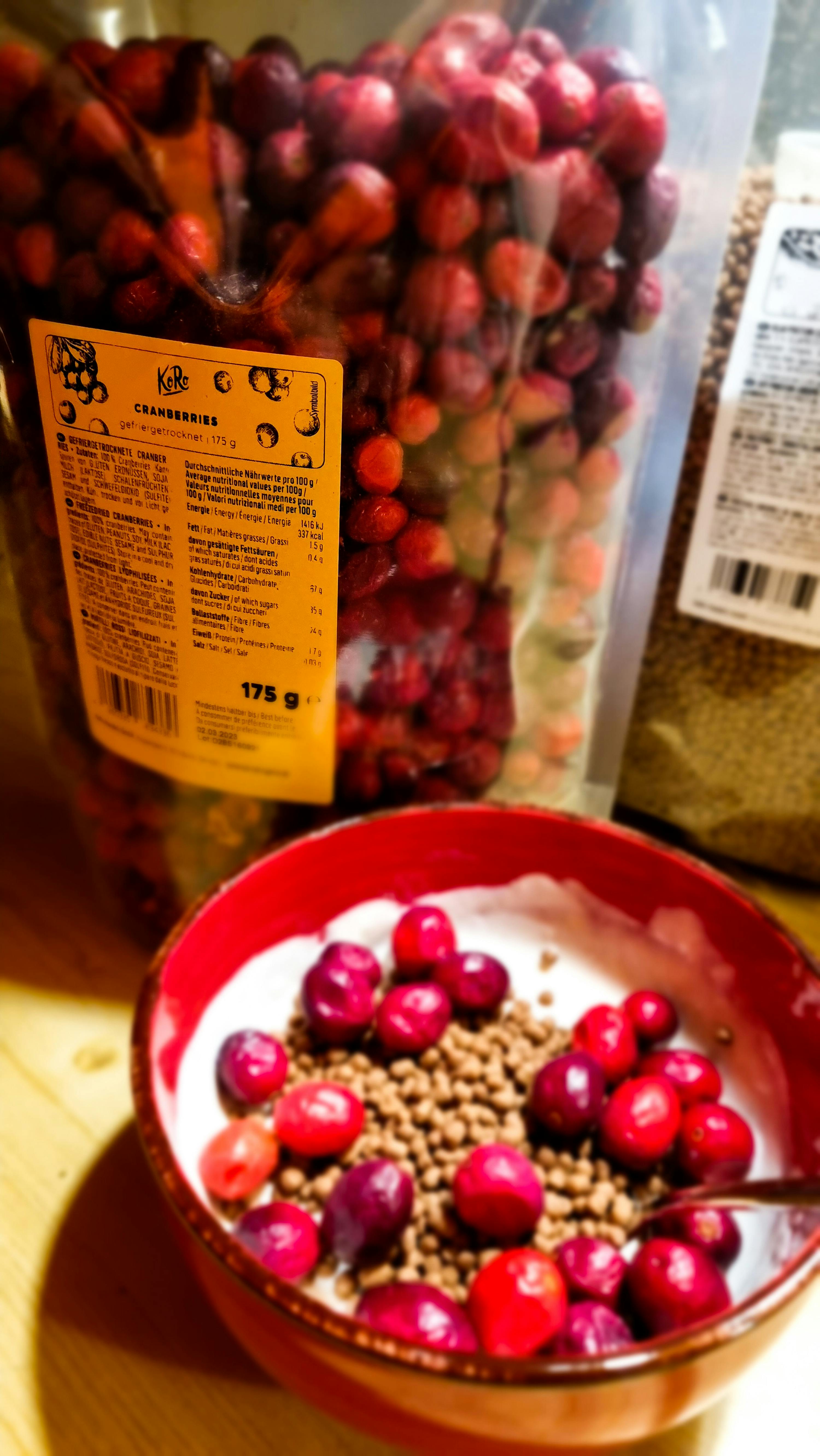 eine rote schüssel mit joghurt und cranberries neben einem sack cranberries