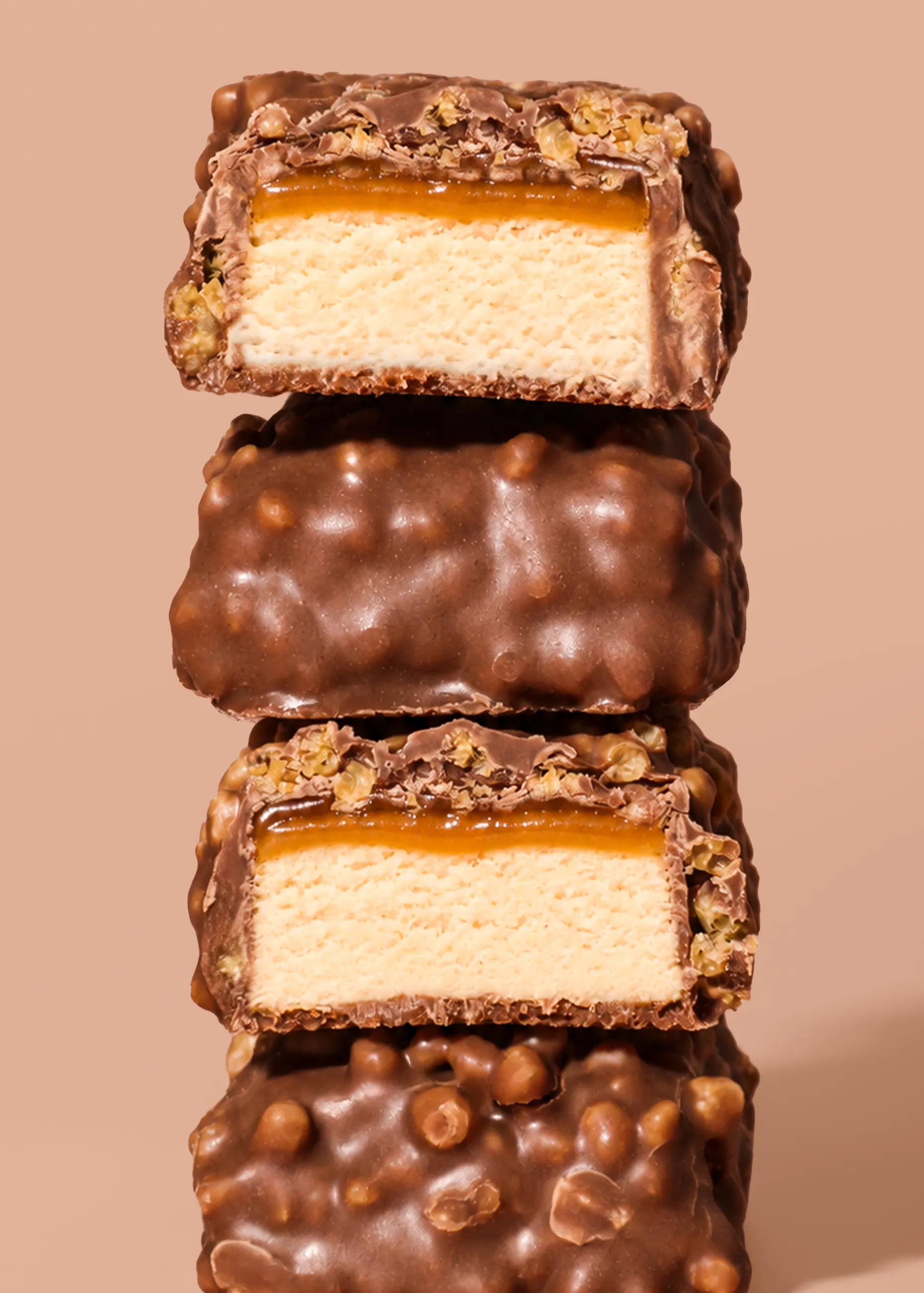 a stack of two chocolate-covered bars, both cut in half to reveal a creamy light-colored filling, a caramel layer, and a chocolate coating with crunchy pieces.