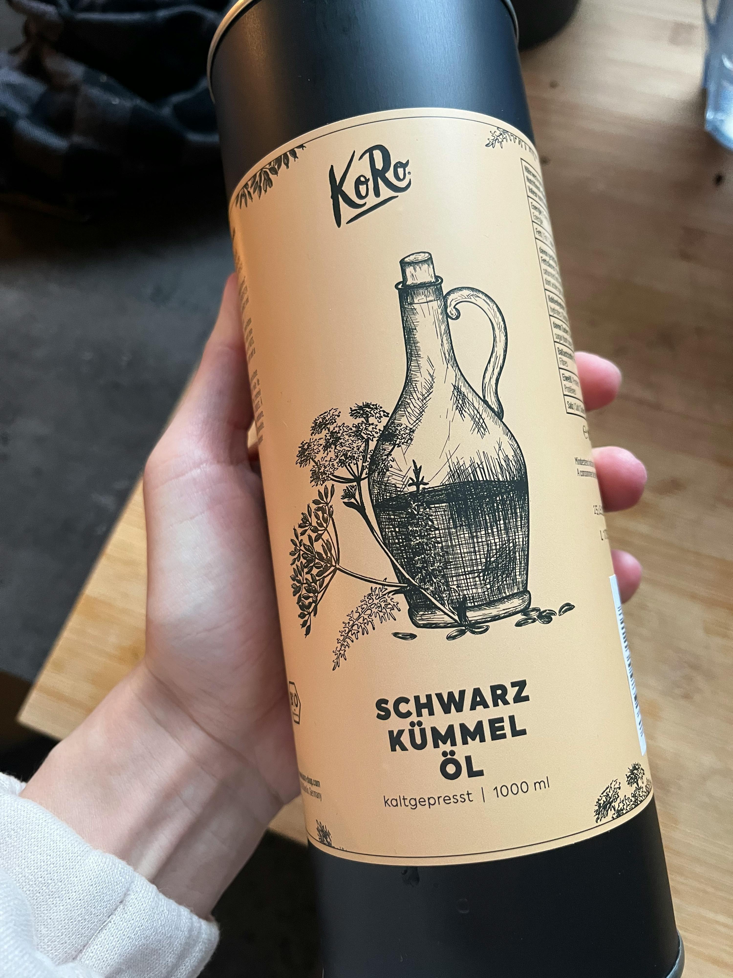 eine Person hält eine Flasche schwarzem Kummelöl in ihrer Hand